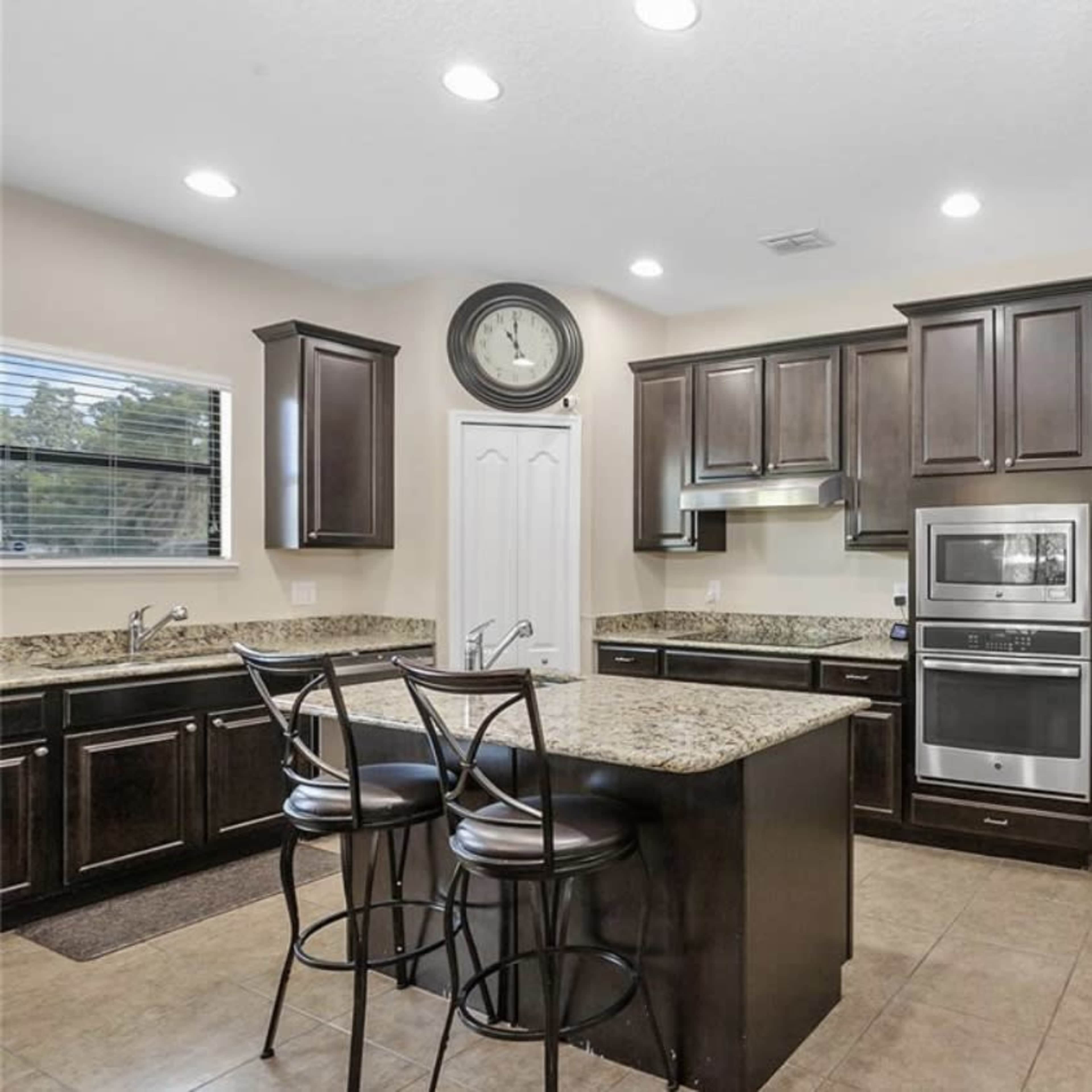 A modern kitchen with dark wooden cabinets, granite countertops, and stainless steel appliances, including an oven and refrigerator.
