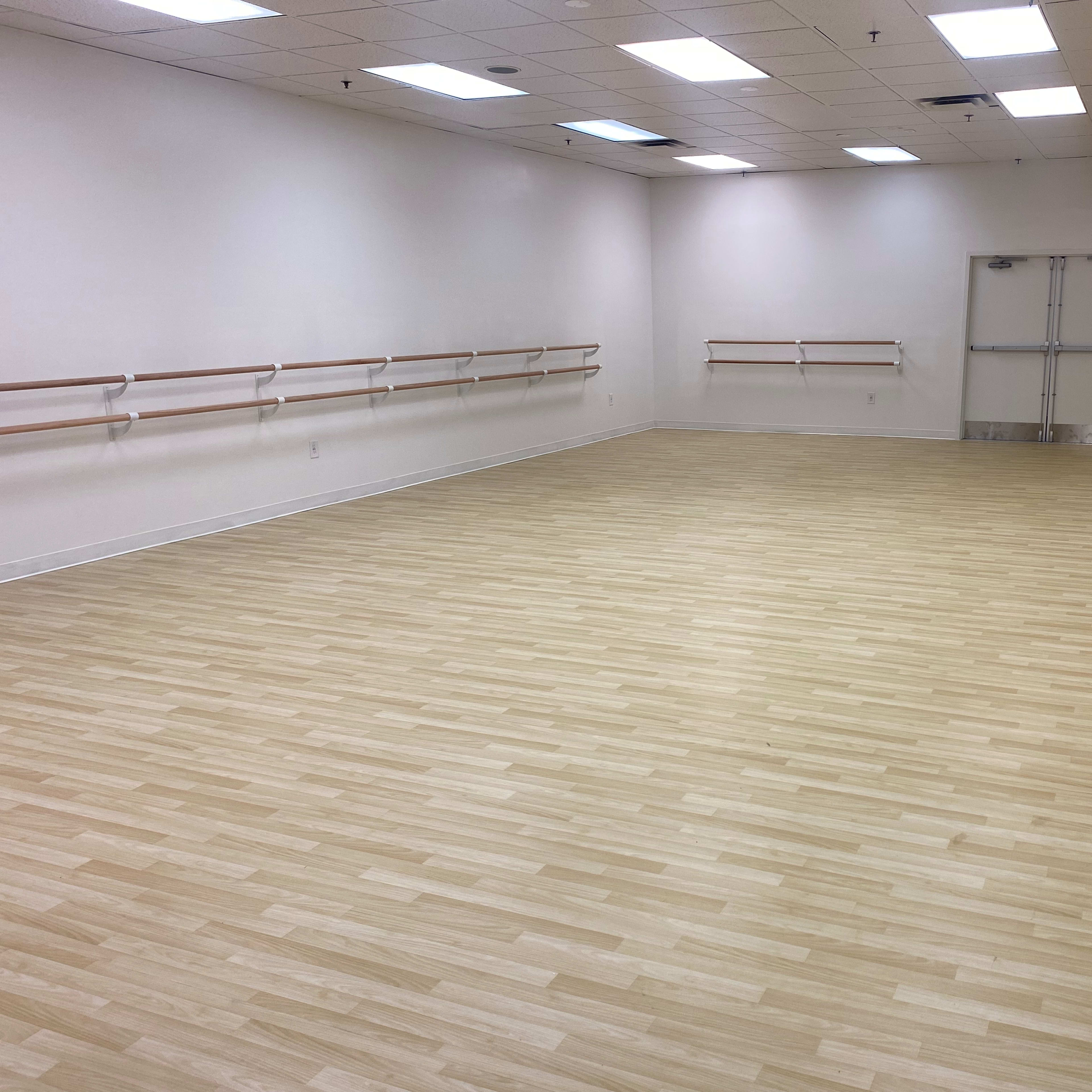 A dance studio with wooden flooring, mirrored walls, and barre installations along one side.