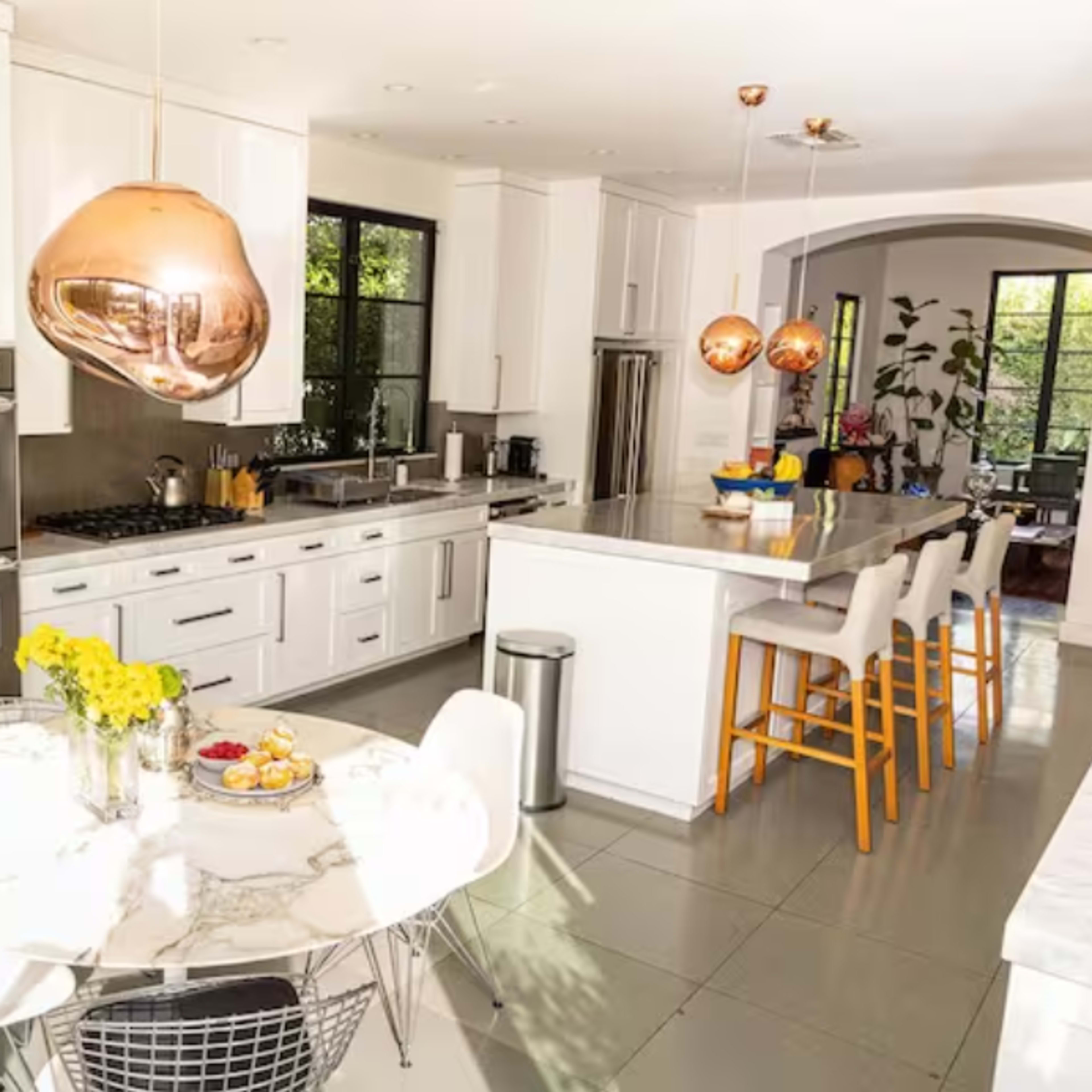 A modern kitchen with white cabinets, a large island, and a marble dining table decorated with flowers and fruit.
