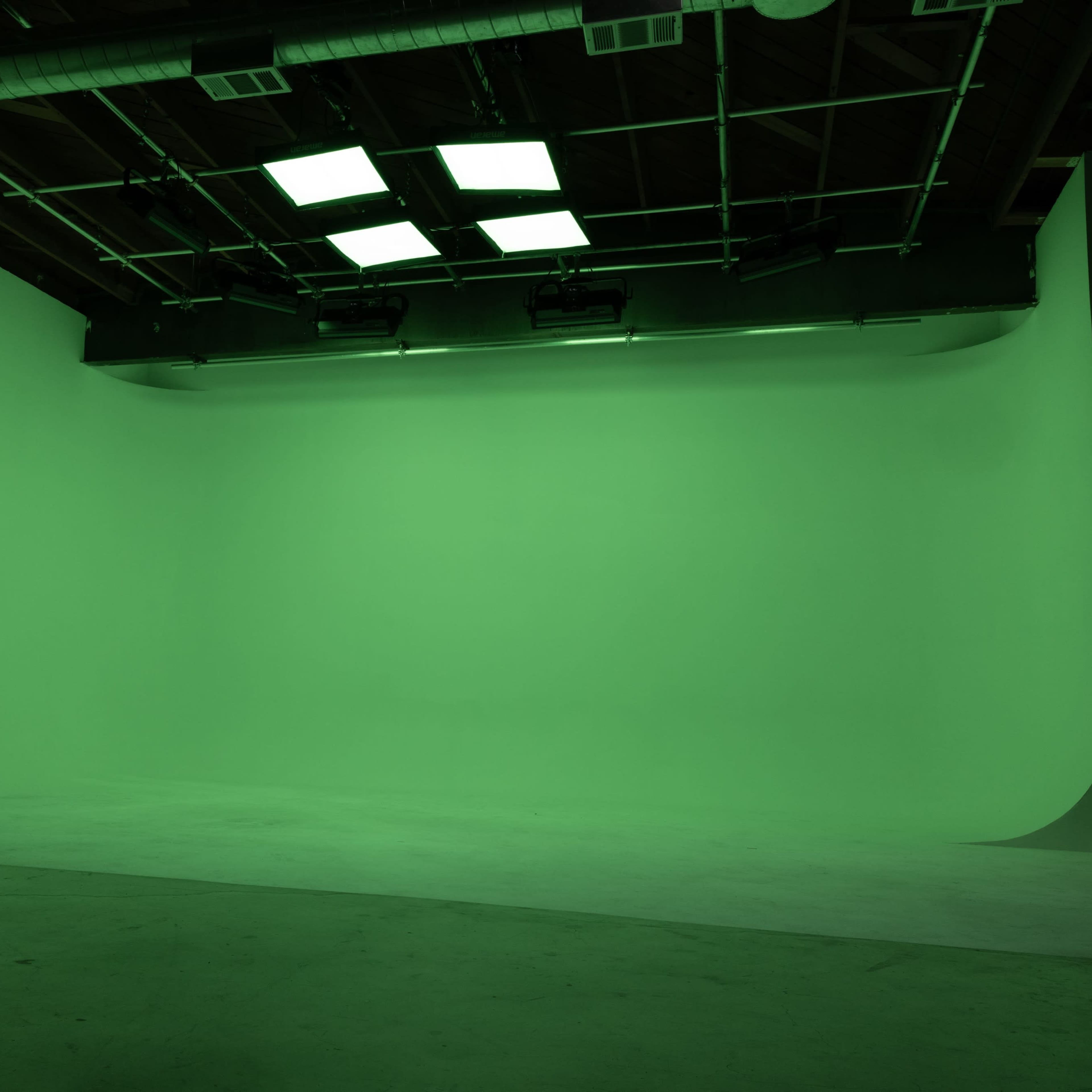 A brightly lit studio space features a seamless green backdrop and a polished concrete floor.