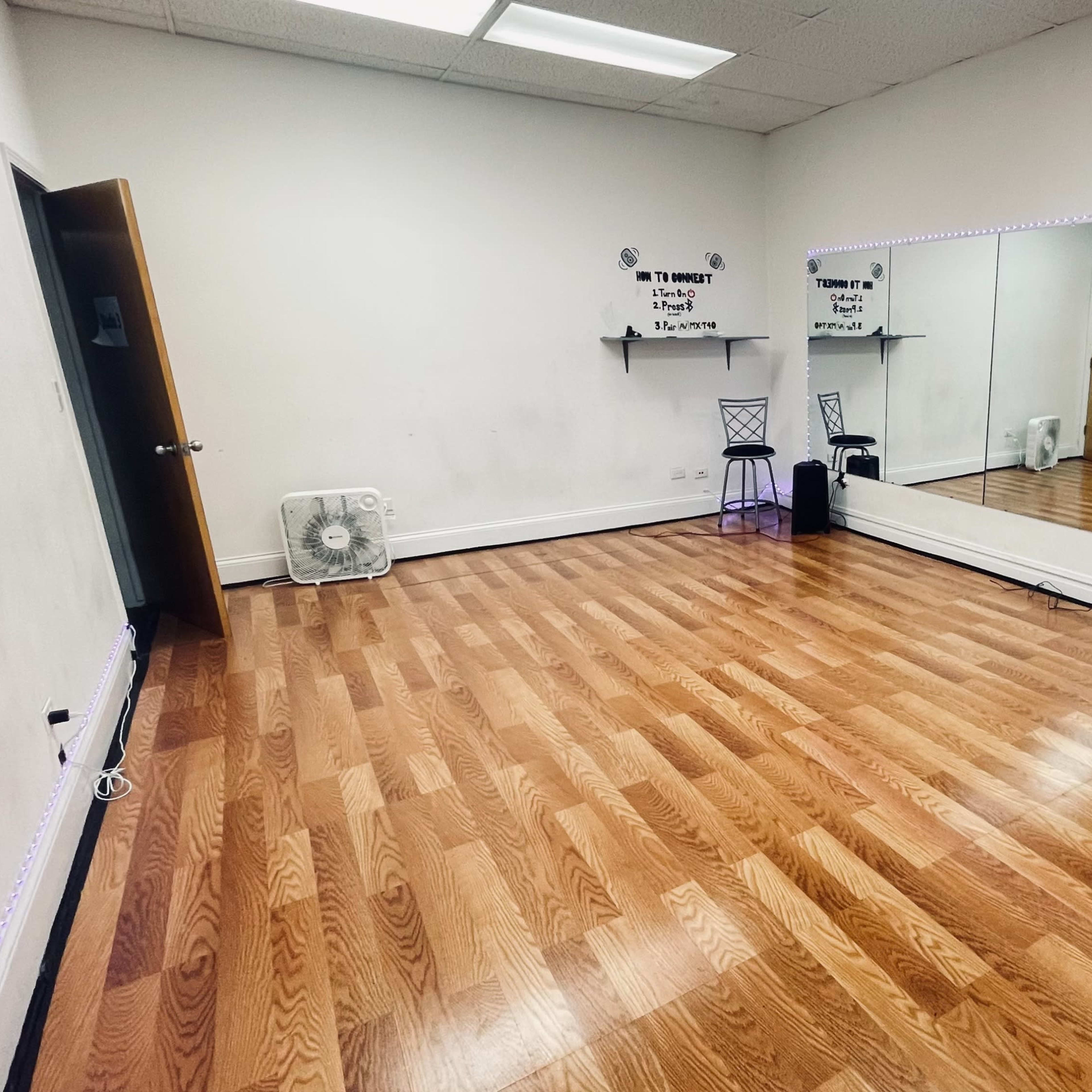 An empty studio room with wooden flooring, a wall-mounted mirror, and minimal decorations.