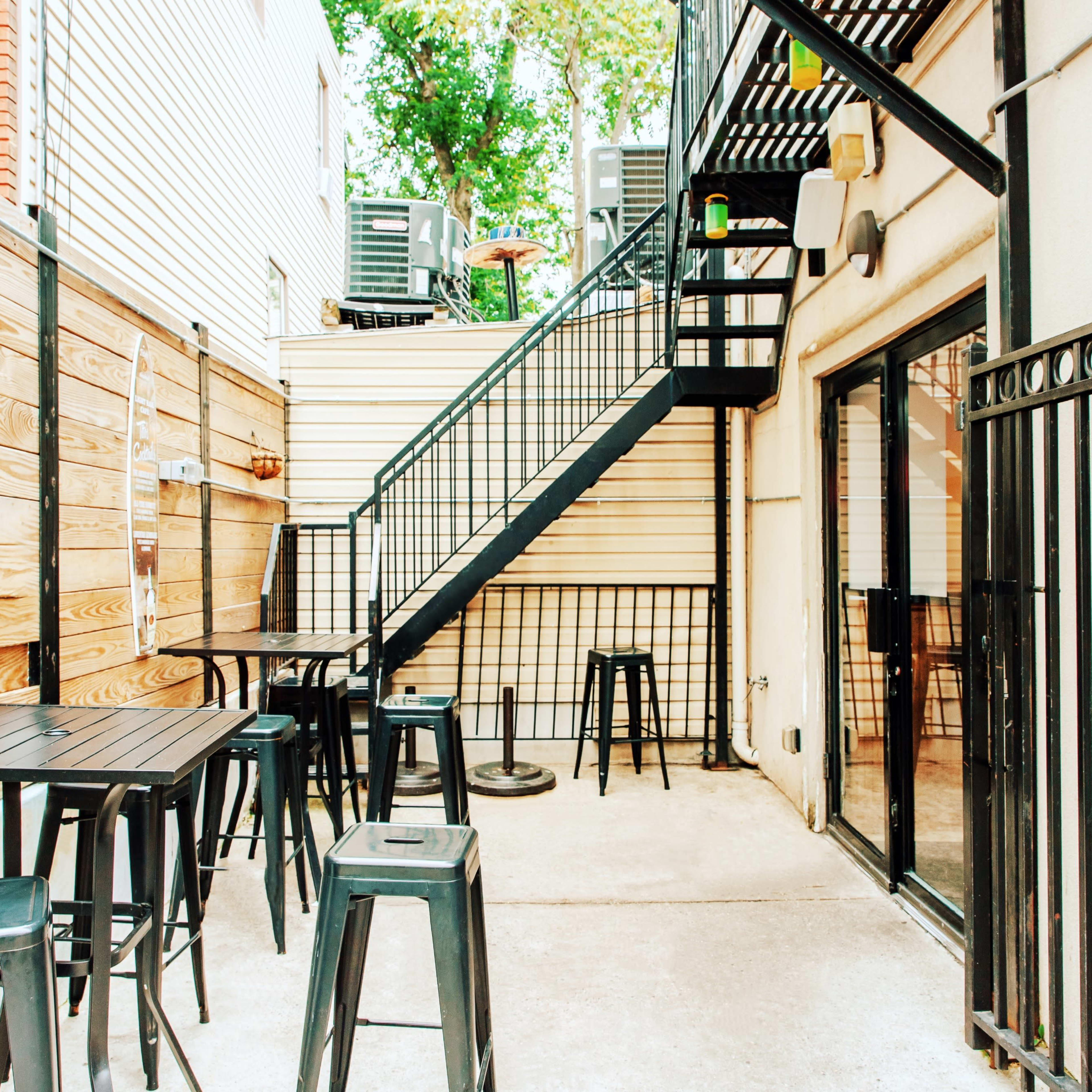 A small outdoor seating area with black metal tables and stools next to a staircase and wooden fences.