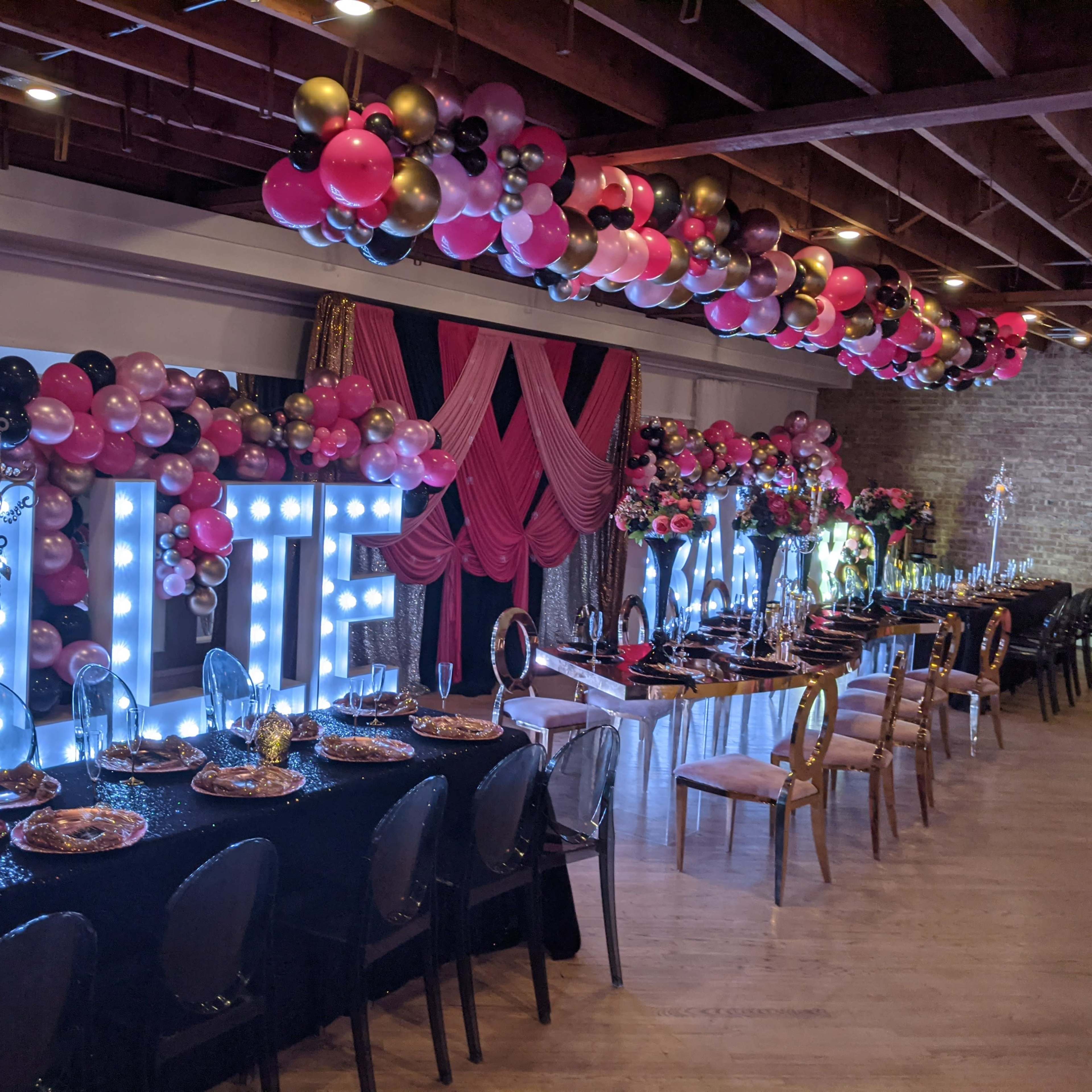 A decorated event space featuring large illuminated letters spelling "BLUE" and an elegantly set table adorned with balloons and stylish decor.