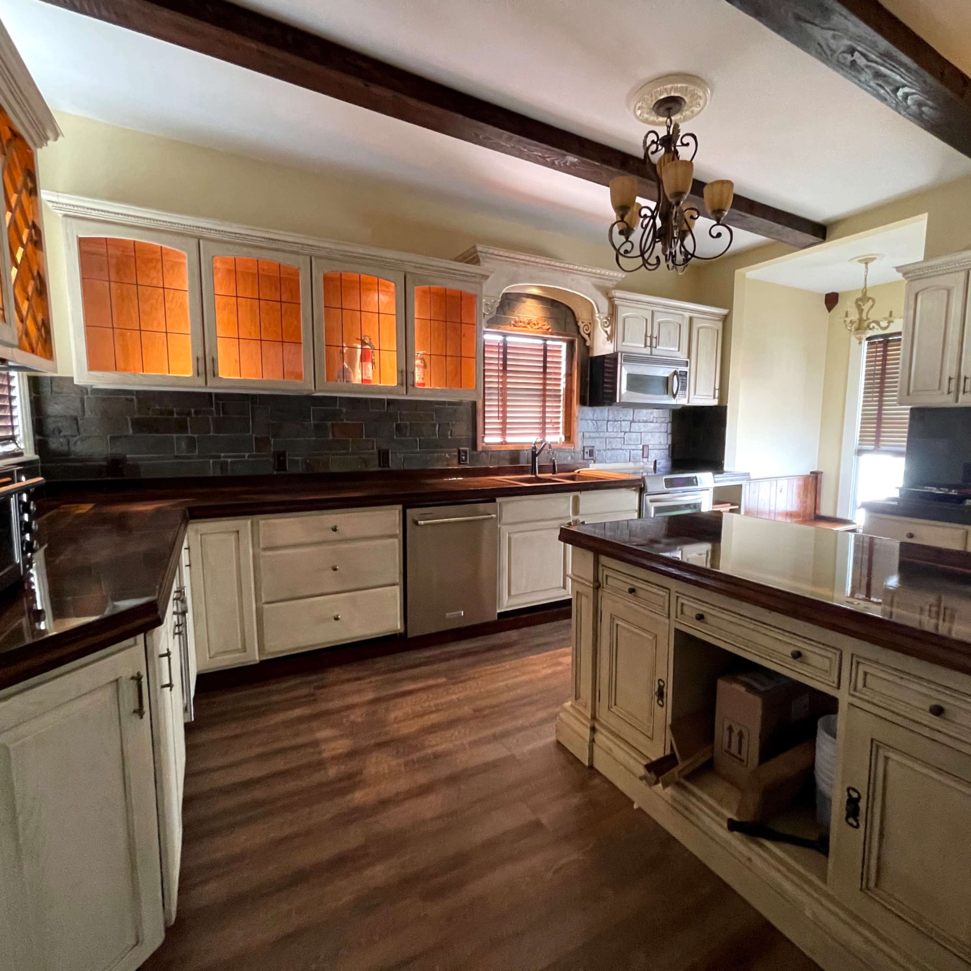 The kitchen features wooden cabinets with glass inserts, a central island, and stainless steel appliances, all set against a backdrop of dark stone walls.