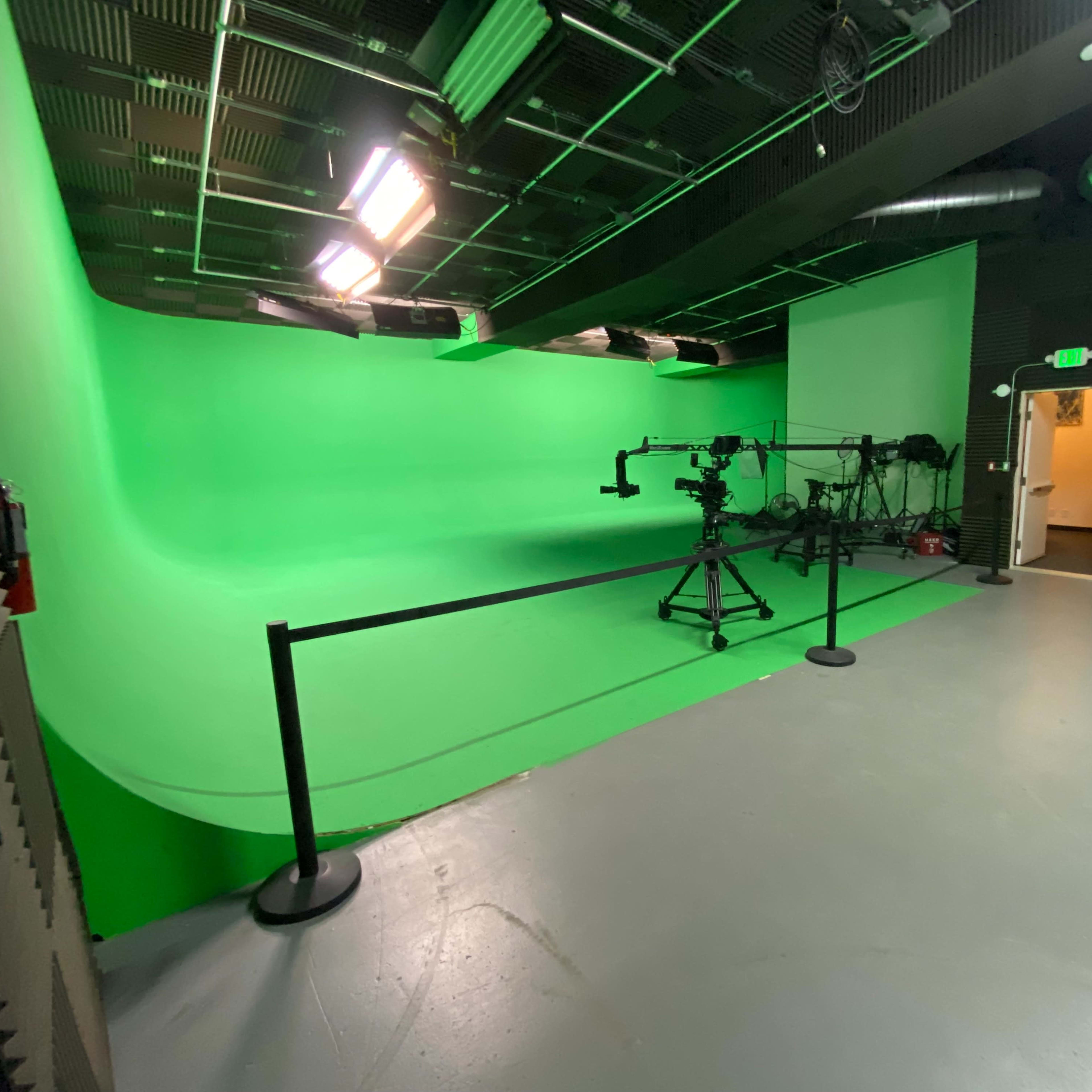 A green screen studio equipped with a camera on a tripod and various lighting setups.