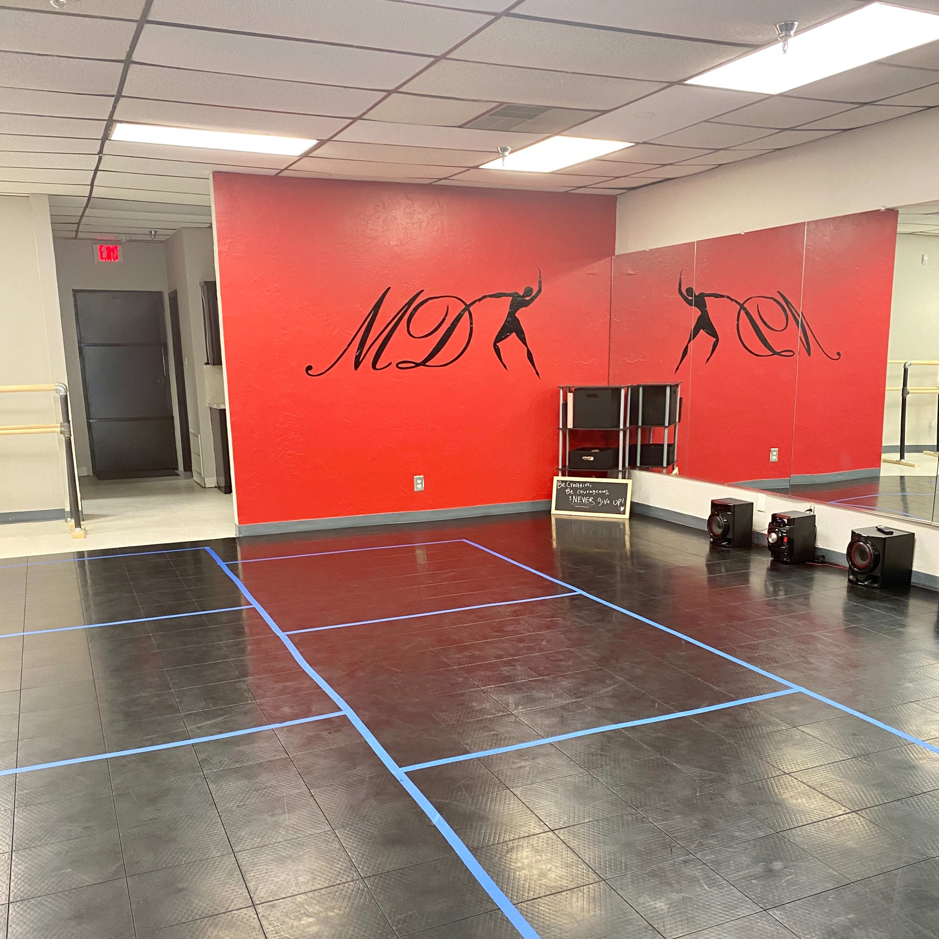 A dance studio with a mirrored wall, red accents, and a floor marked by blue tape in a grid pattern.