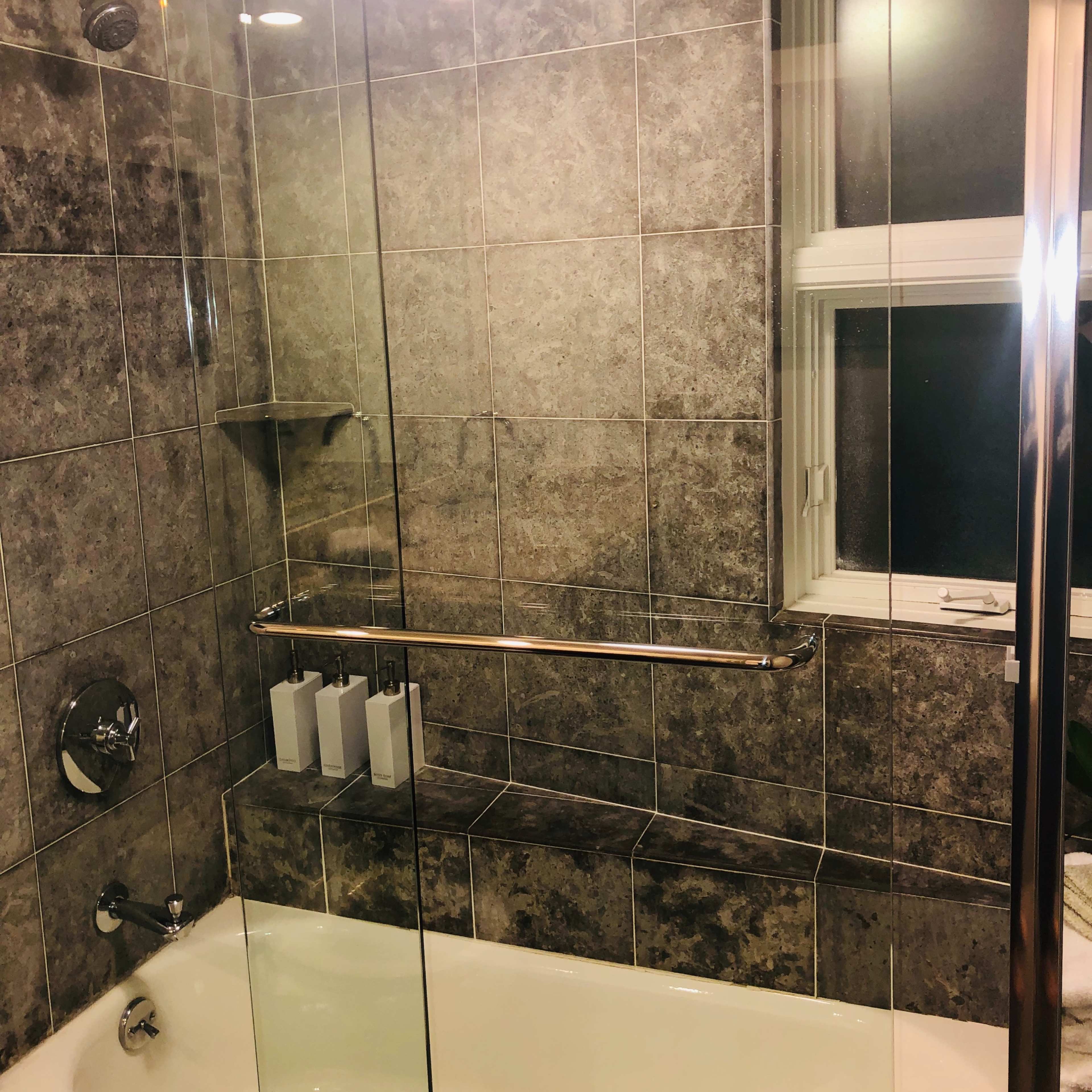 A tiled bathroom with a glass shower enclosure, a bathtub, and a window.
