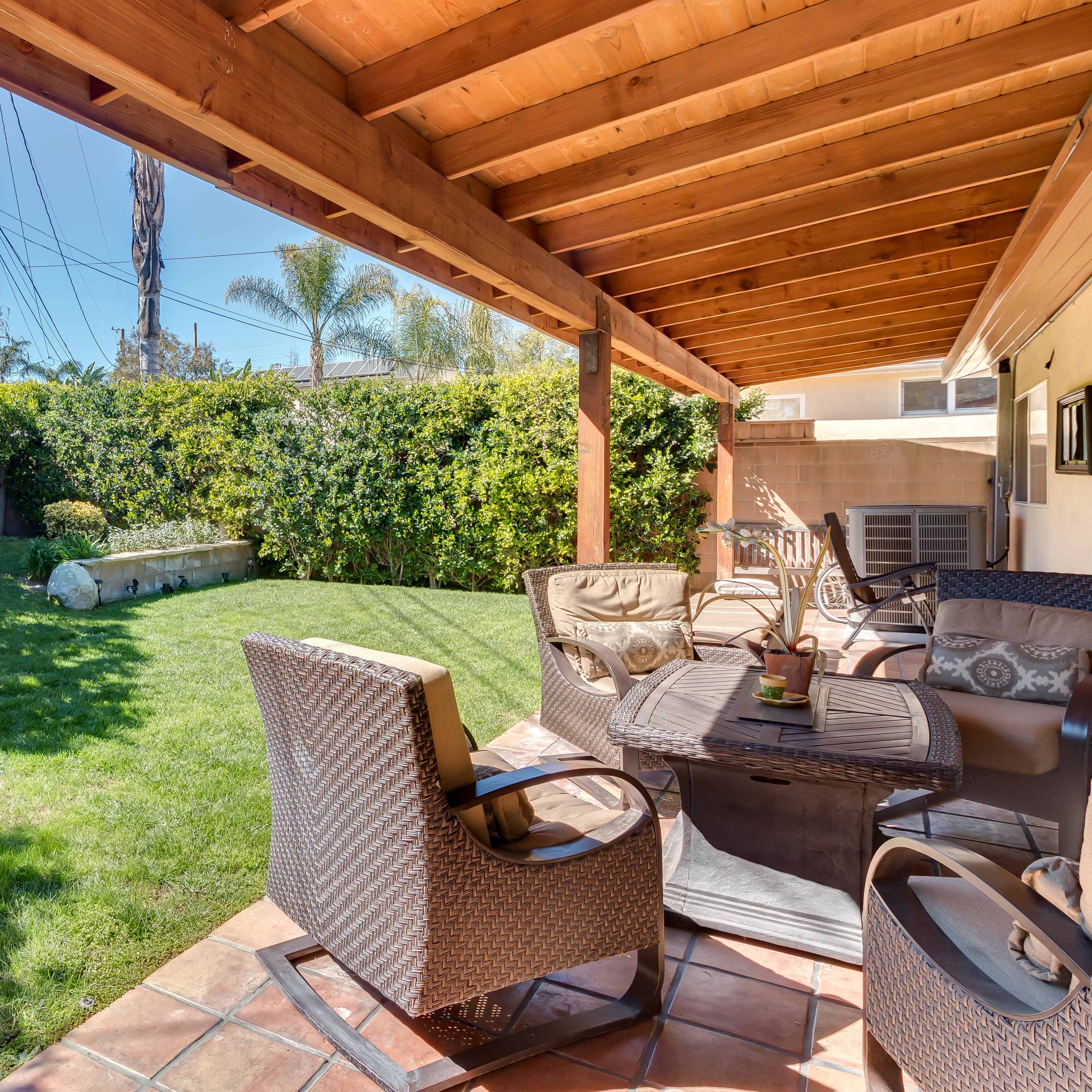 A patio area features outdoor seating and a landscaped garden with green grass and hedges under a wooden roof.