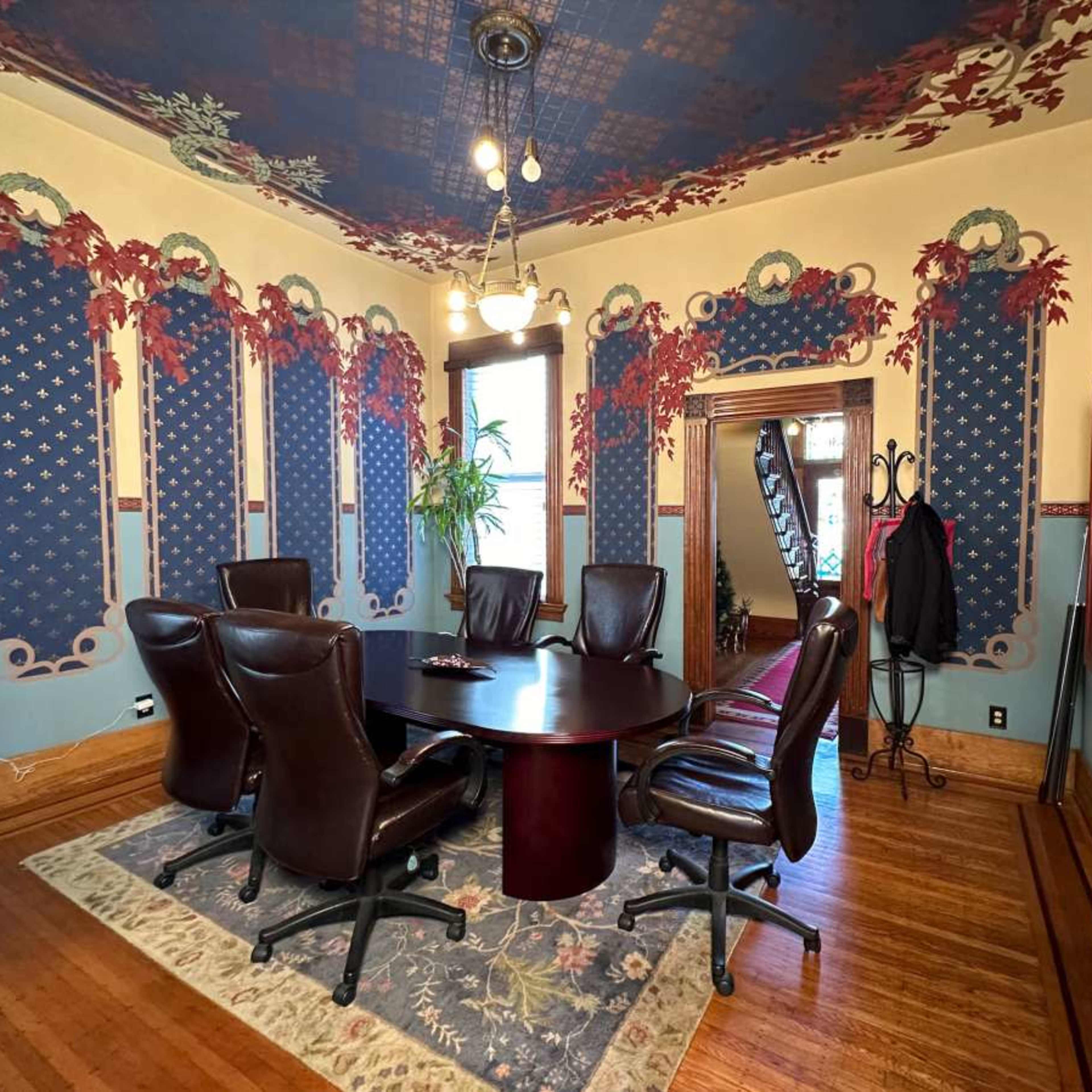 A conference room with a round table surrounded by black leather chairs, characterized by decorative wallpaper and a patterned ceiling.