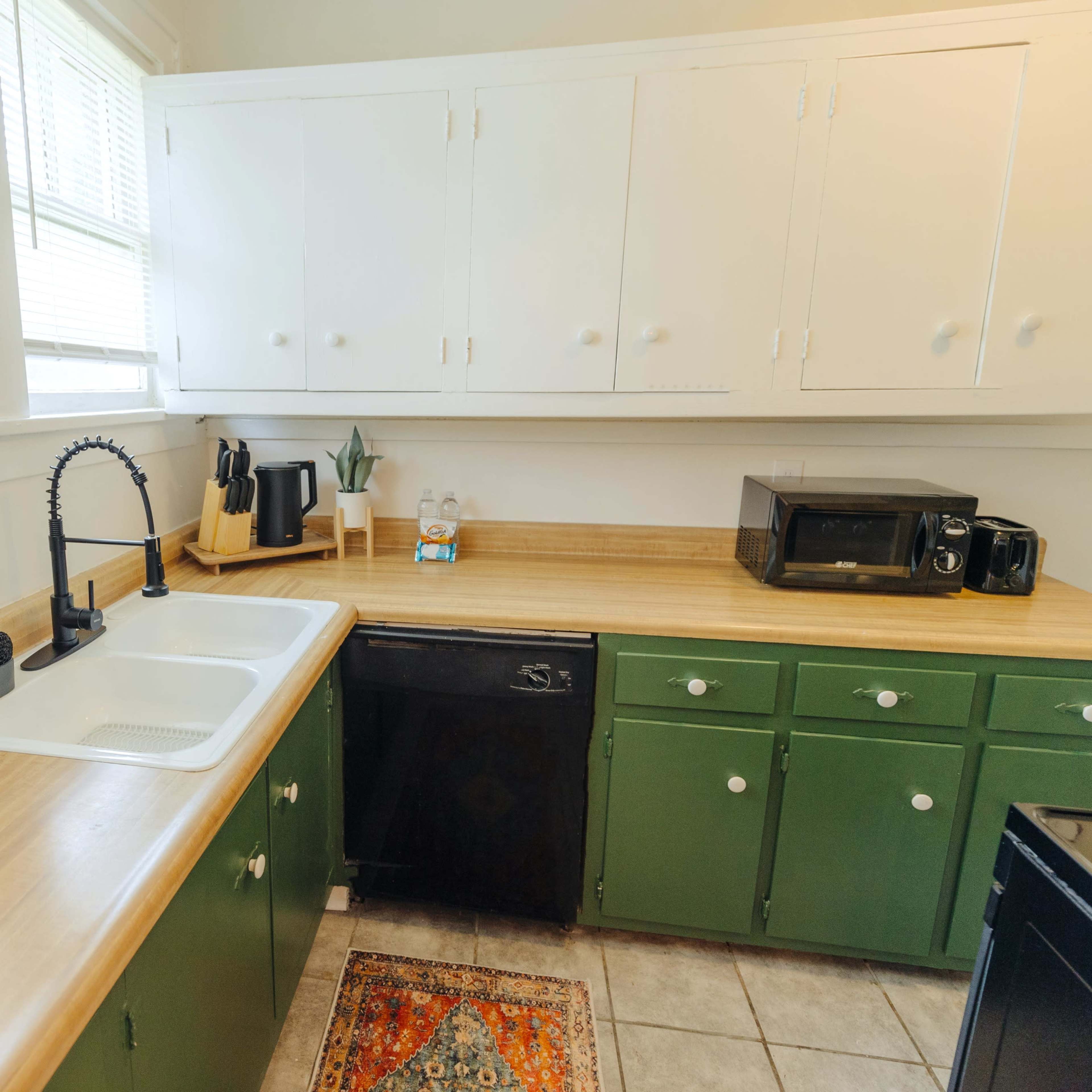 A small kitchen features a sink with a modern faucet, wooden countertops, a black dishwasher, and green cabinets.