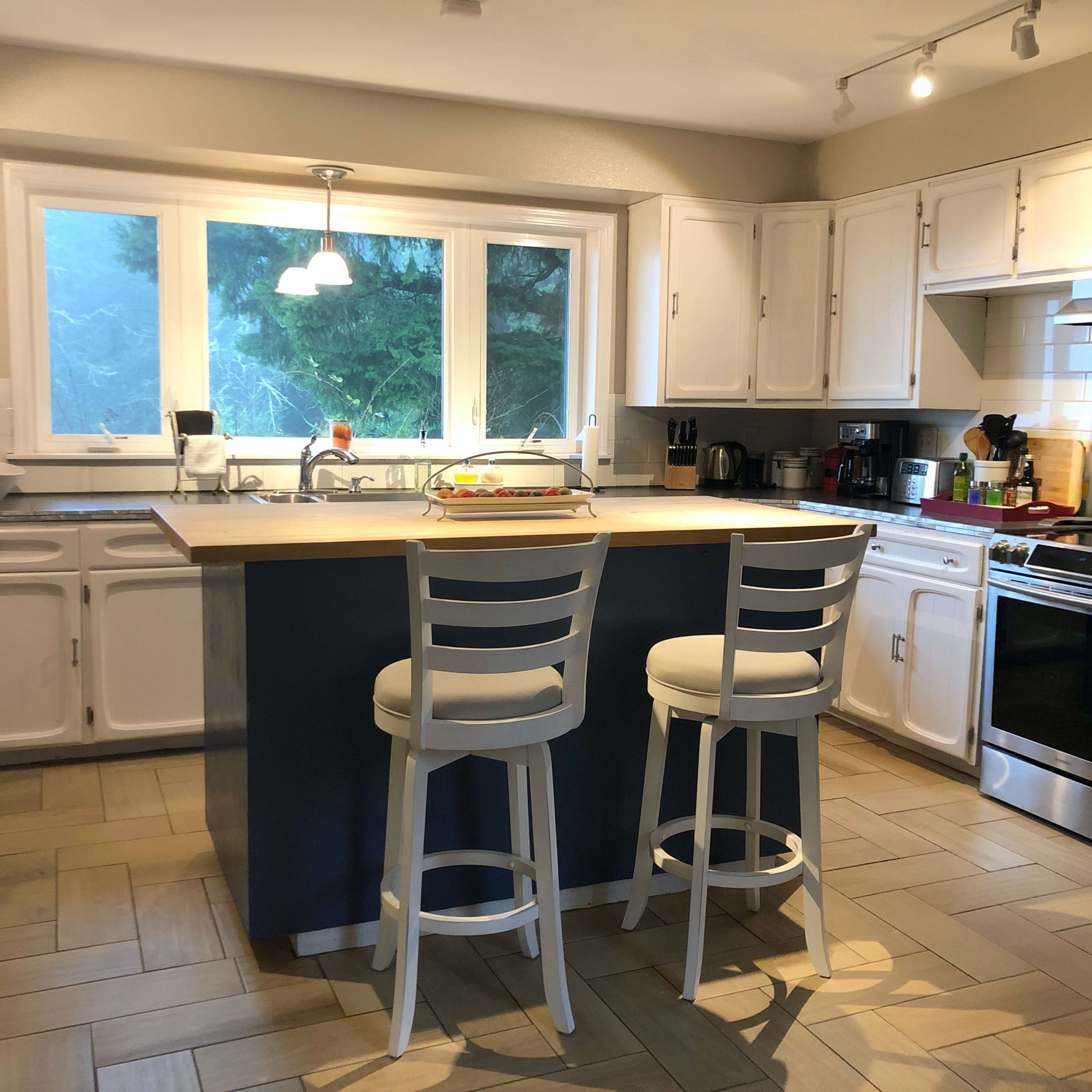 A modern kitchen with white cabinetry, a central island with two stools, and stainless steel appliances.