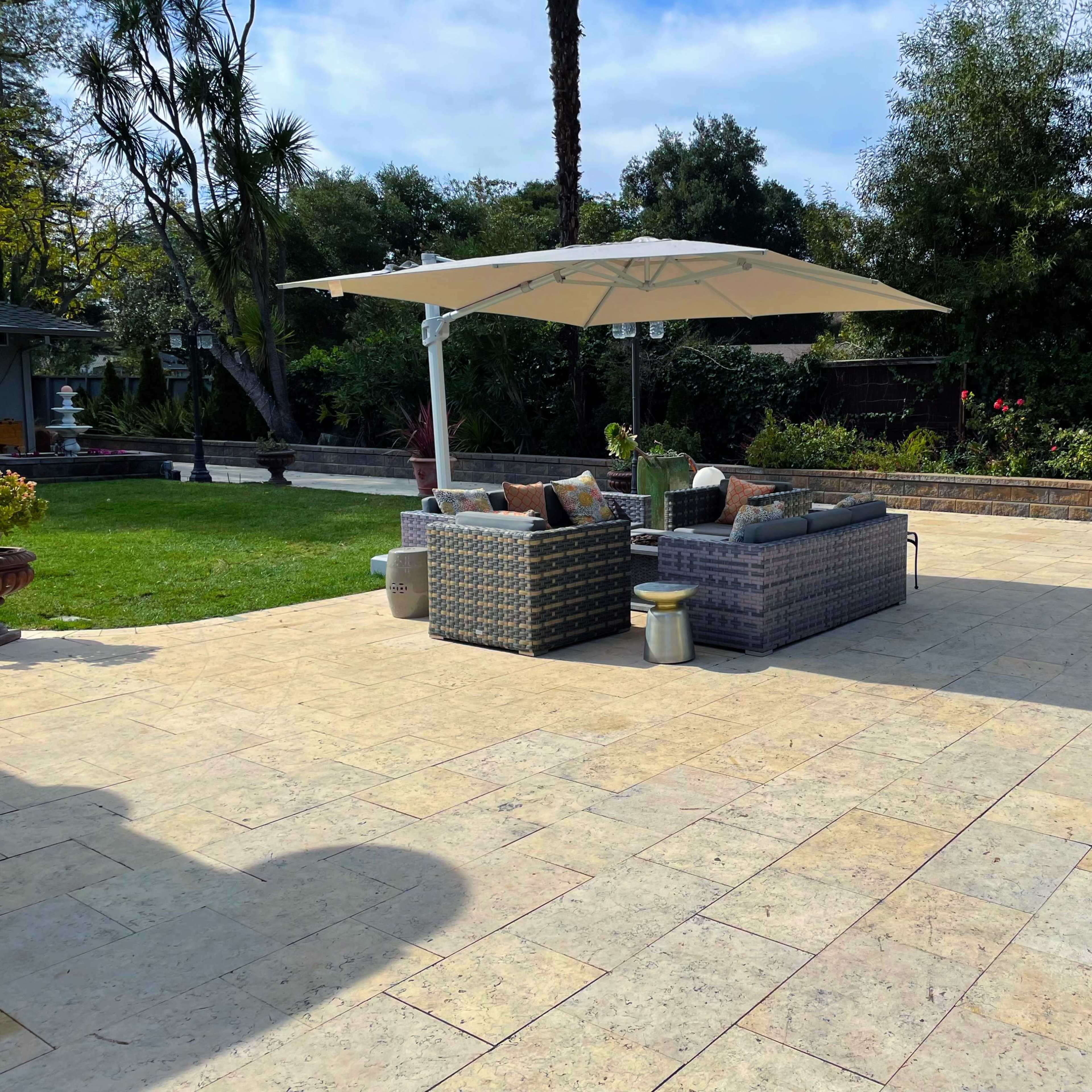 A landscaped outdoor area with a seating arrangement under a large umbrella, surrounded by greenery and decorative plants.