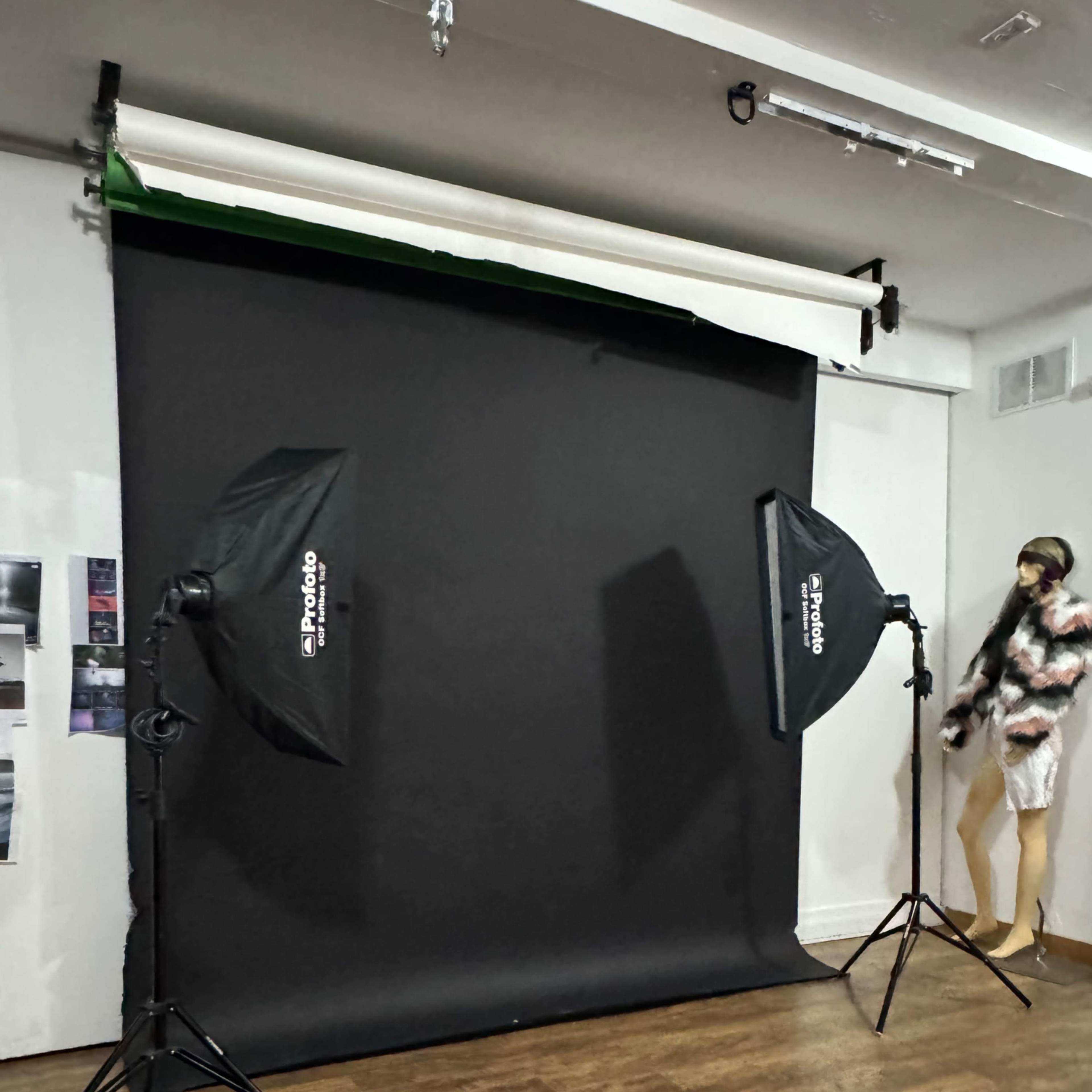 A photo studio setup features two softbox lights on stands flanking a black backdrop, with a mannequin dressed in a fur coat positioned nearby.
