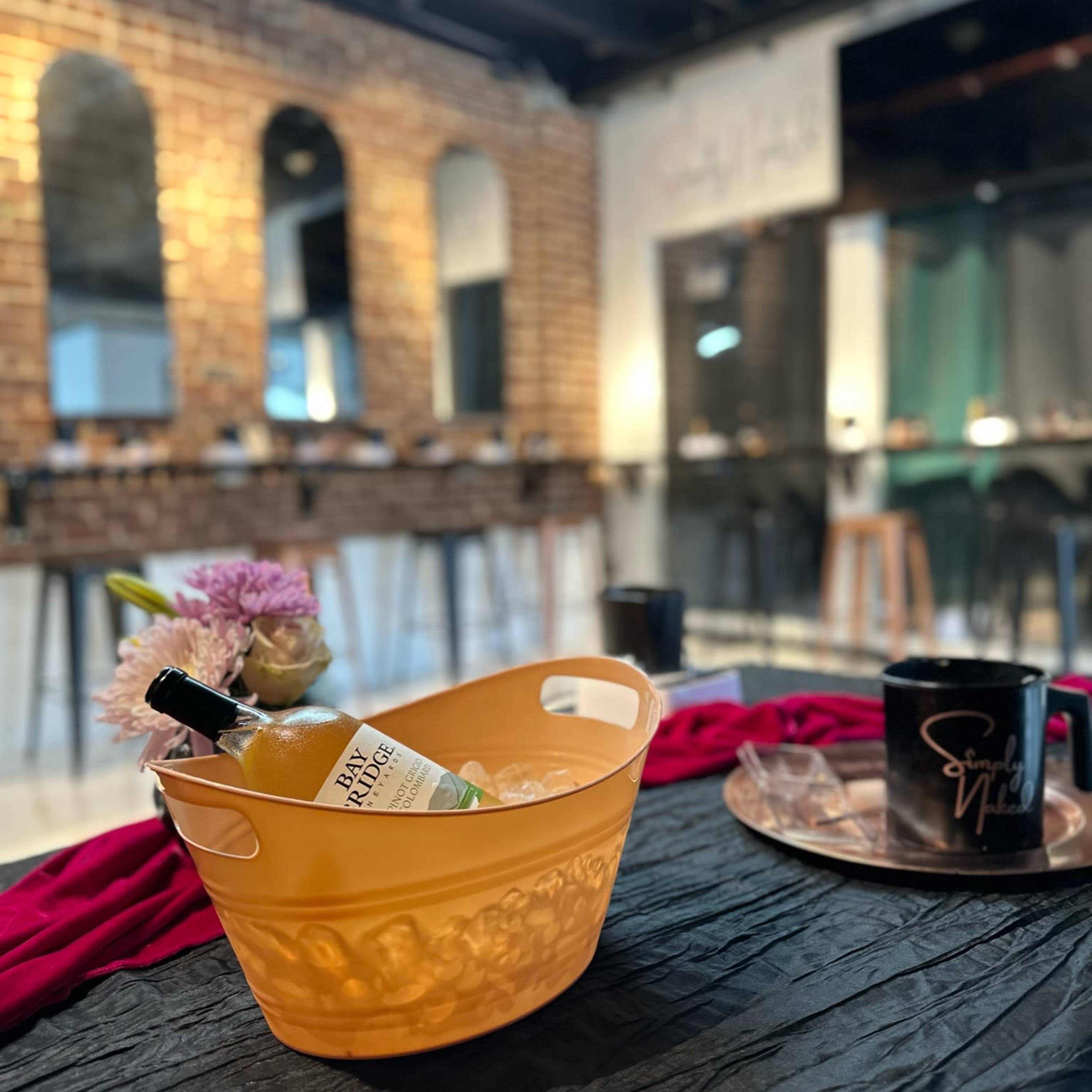 A yellow ice bucket with a bottle and garnishes is centered on a table, set against a backdrop of brick walls and mirrors in a modern interior space.
