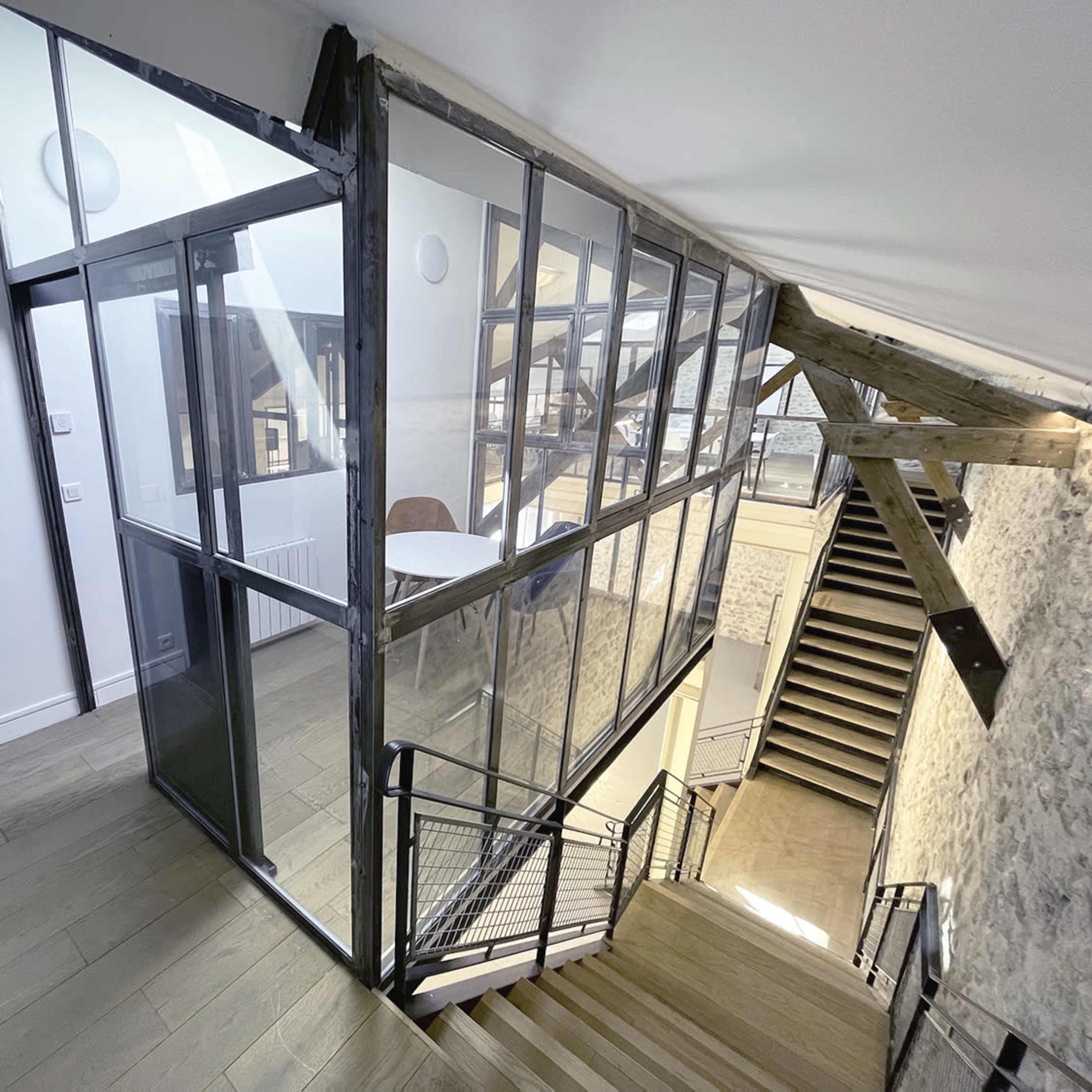 A modern staircase with a glass and metal partition separating different areas of a contemporary interior space featuring exposed stone walls and wooden beams.