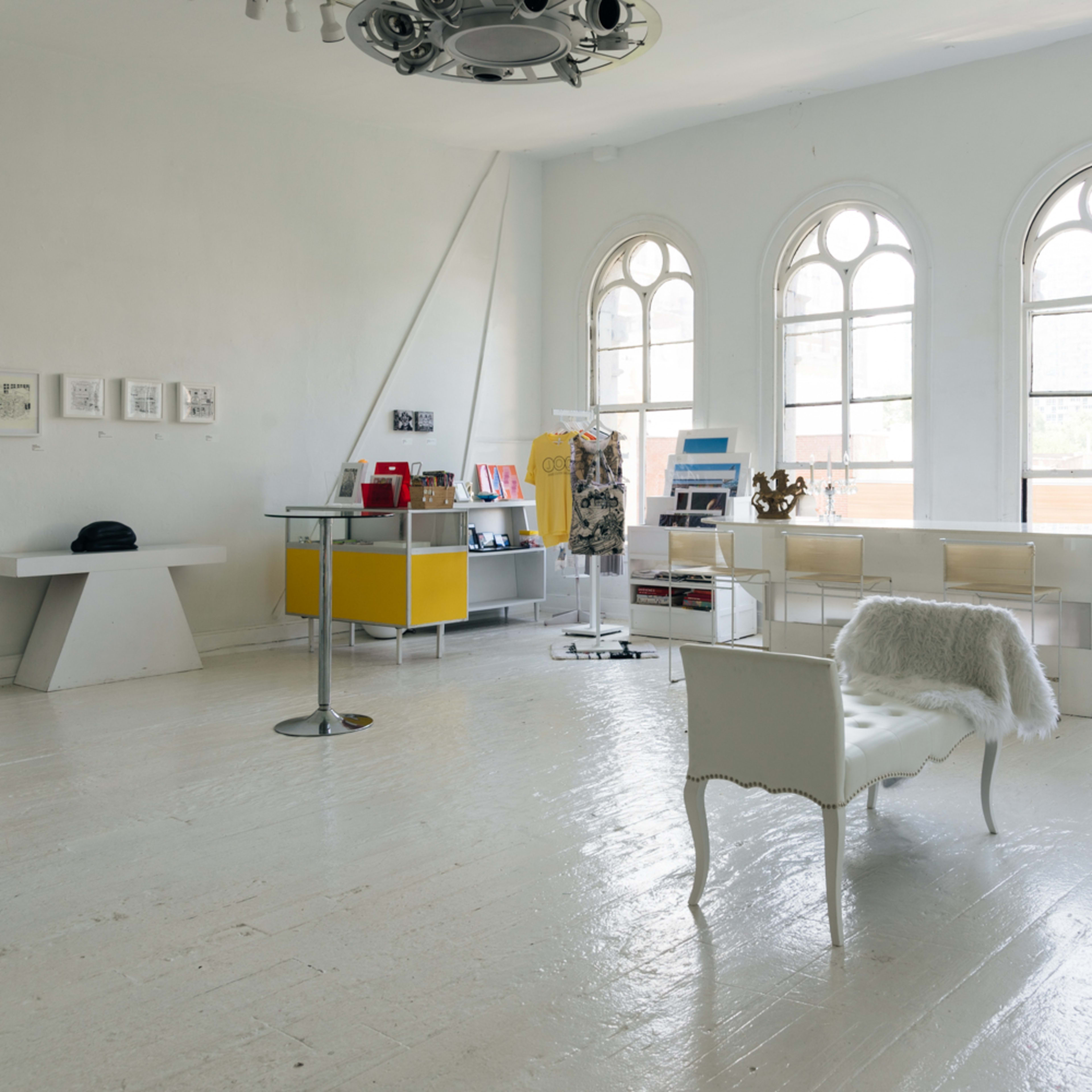 A bright, airy room with large arched windows, featuring minimalist furniture, including a white chair and a modern display table.