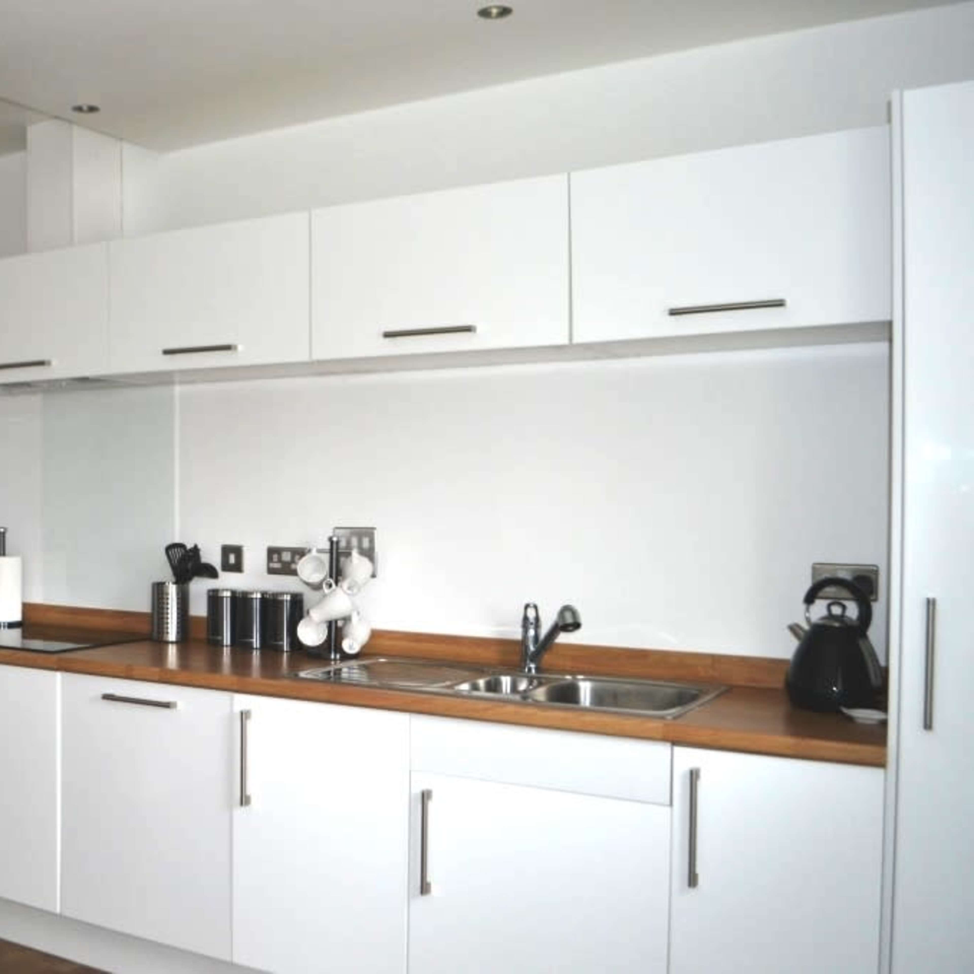 A modern kitchen with white cabinetry, a stainless steel microwave, a sink, and a wooden countertop.