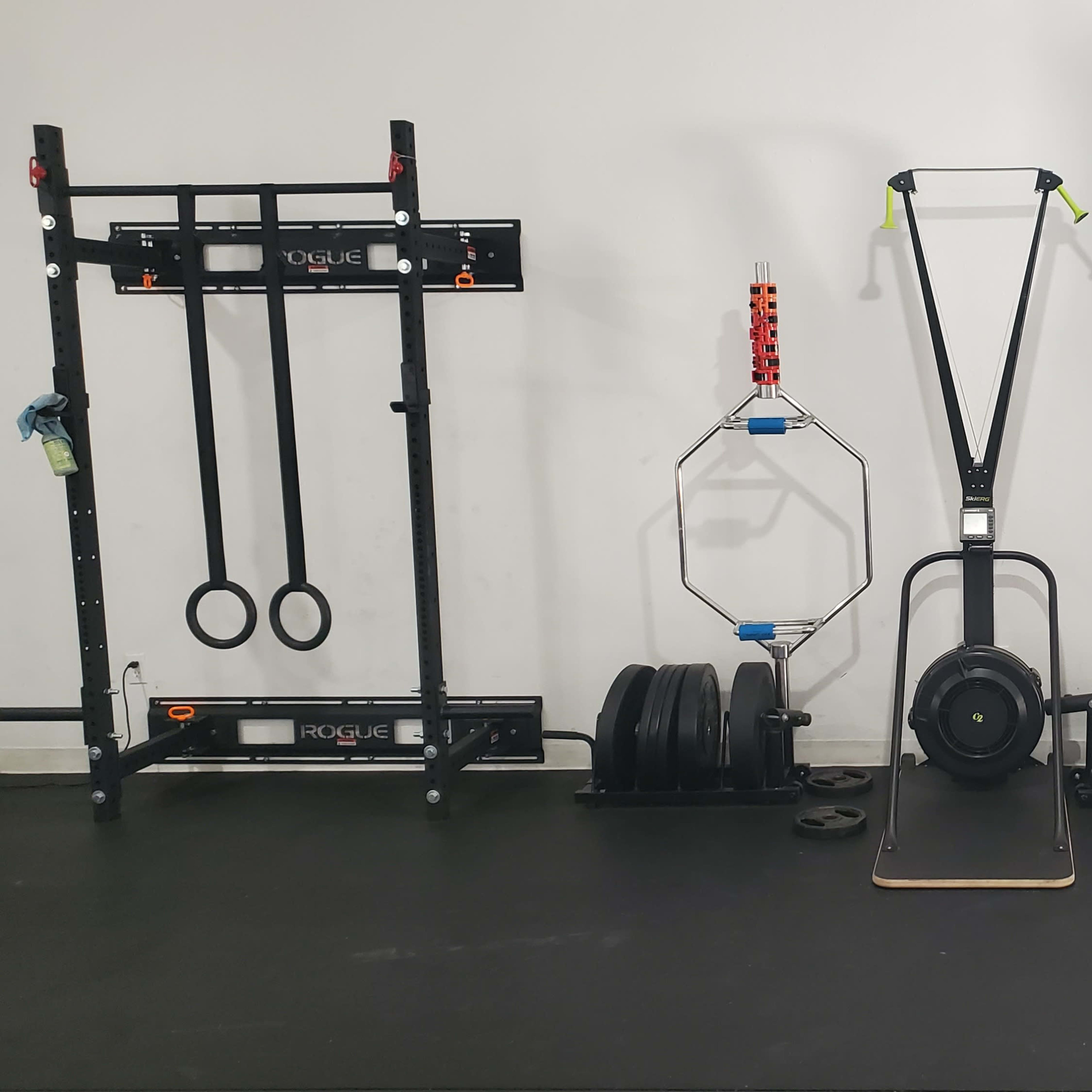 A gym setup featuring a sled push apparatus at the center, flanked by weightlifting racks on both sides, along with various weights and fitness equipment.