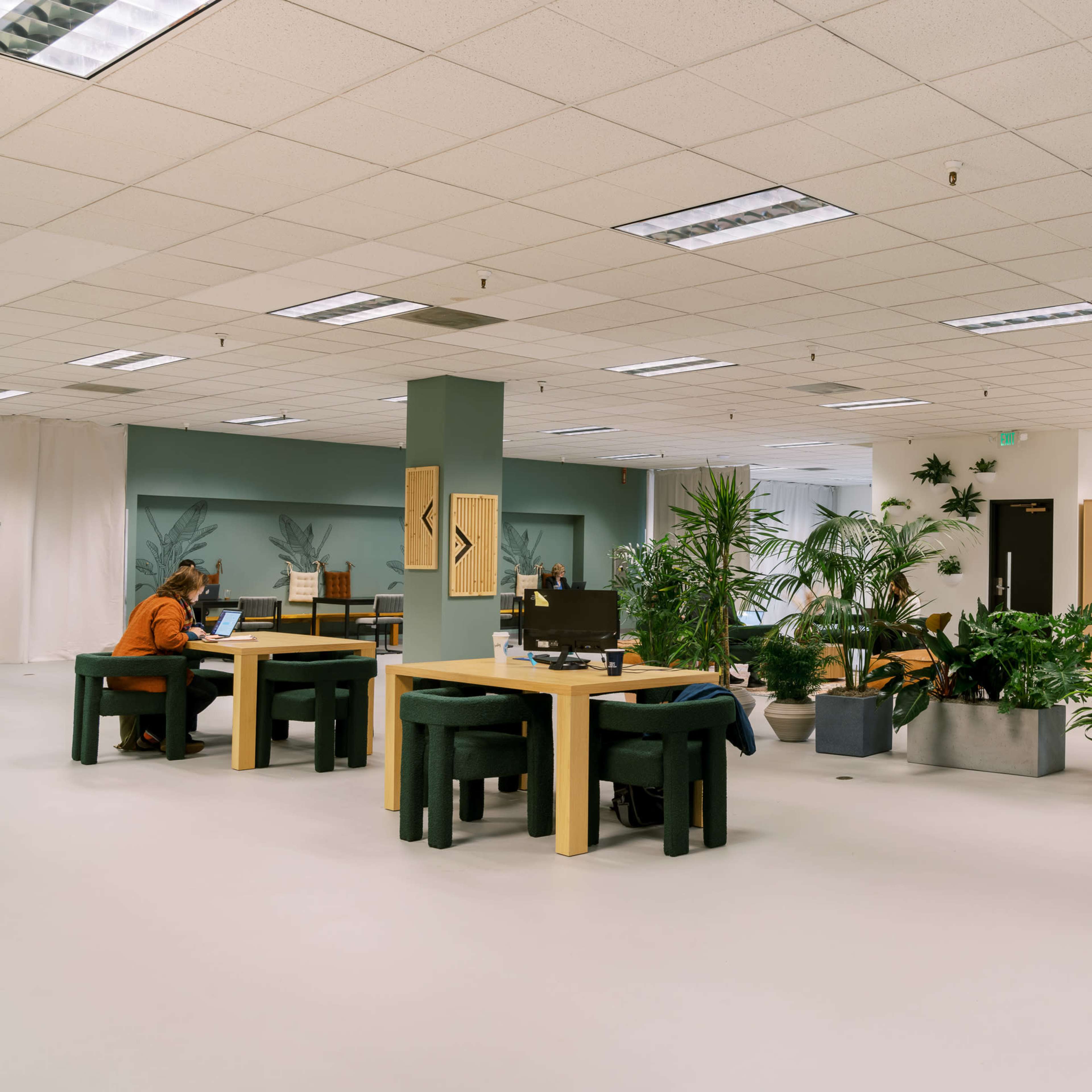 A spacious office environment with several desks, plants, and seating areas for working.