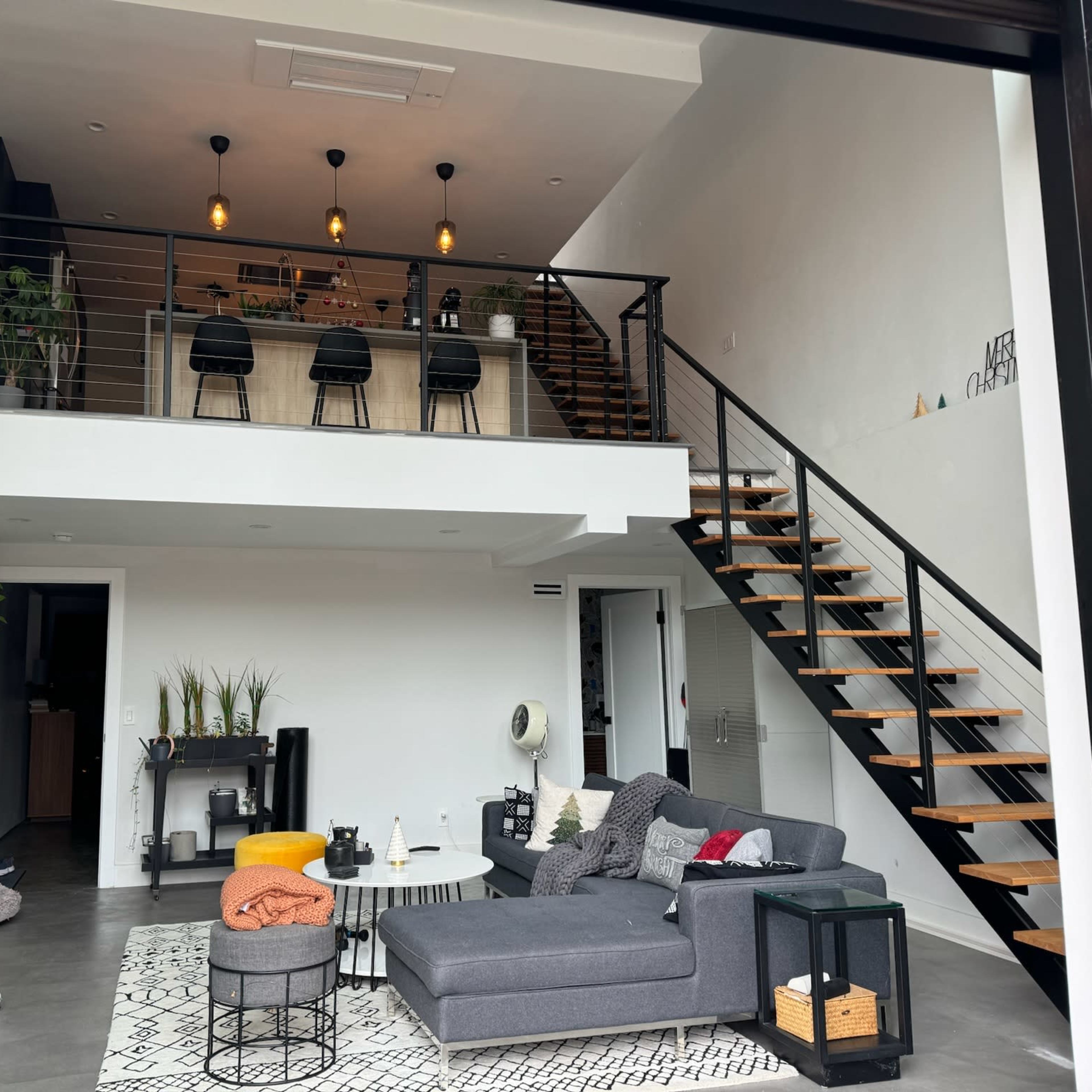 A modern interior space with a two-level layout featuring a living area, a staircase, and a kitchen with bar seating.