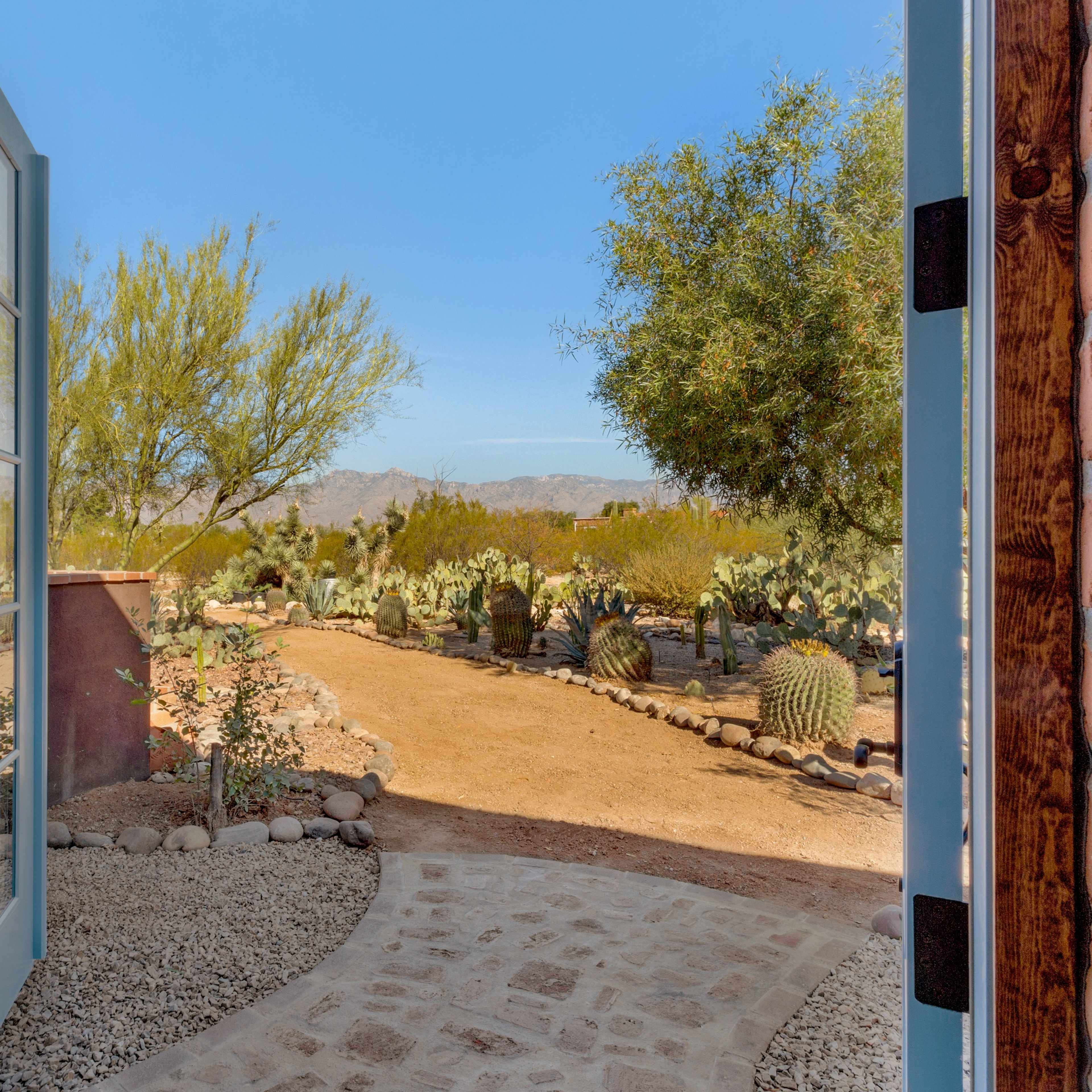 A doorway opens to a desert landscape featuring cacti, trees, and a winding path leading into the distance.
