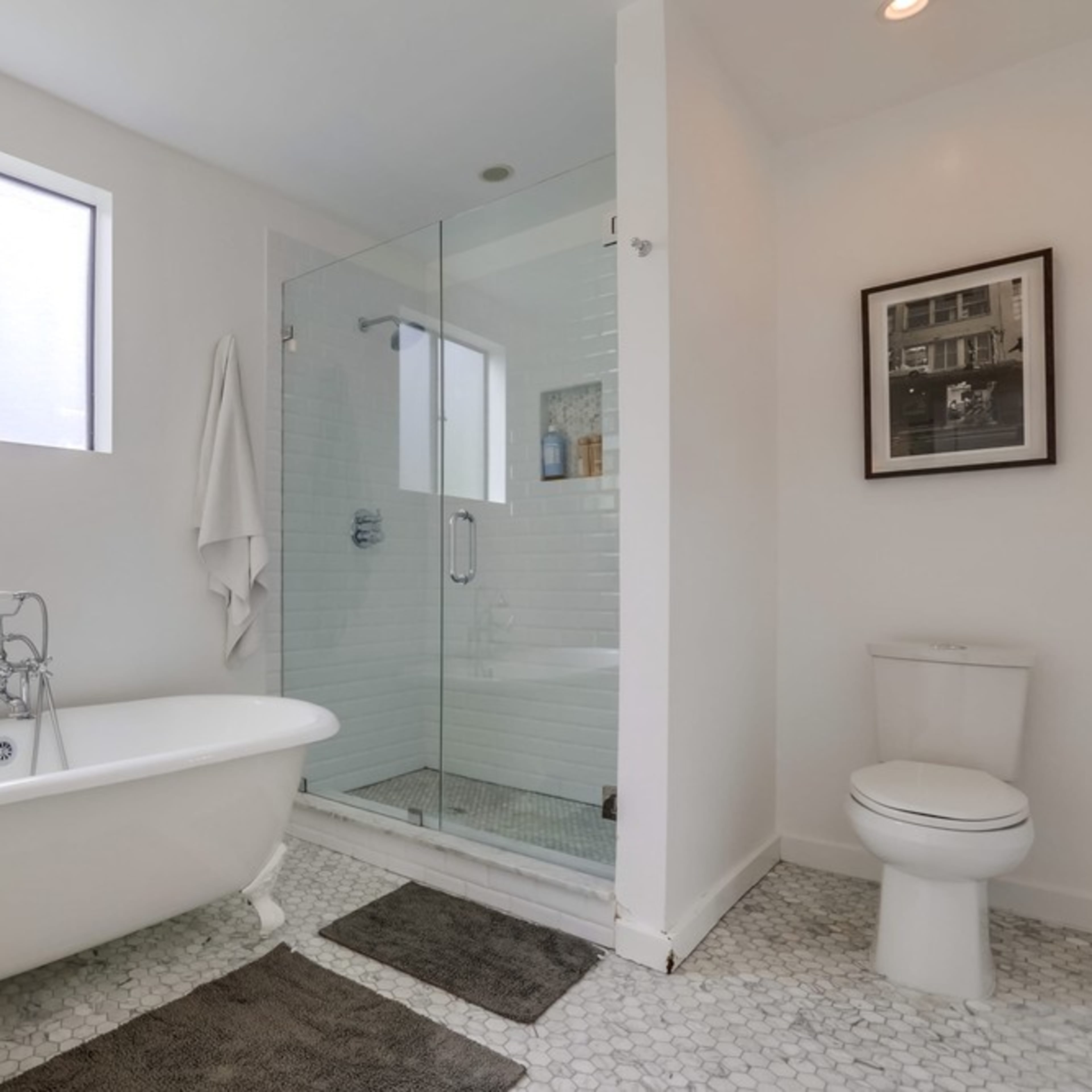 A modern bathroom featuring a freestanding bathtub, a glass shower enclosure, a toilet, and a window.