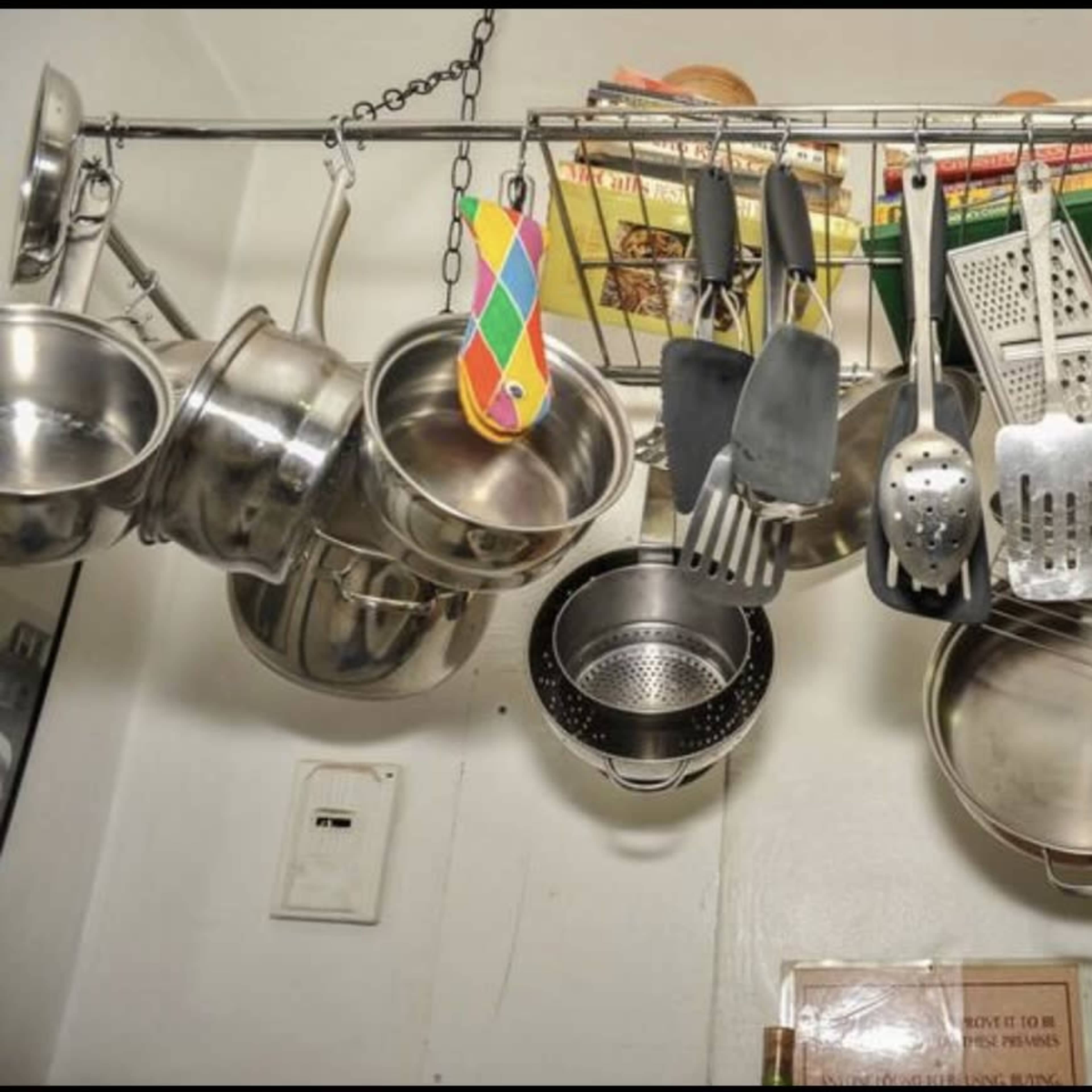 A variety of cooking utensils and pots are suspended from a metal rack in a kitchen.