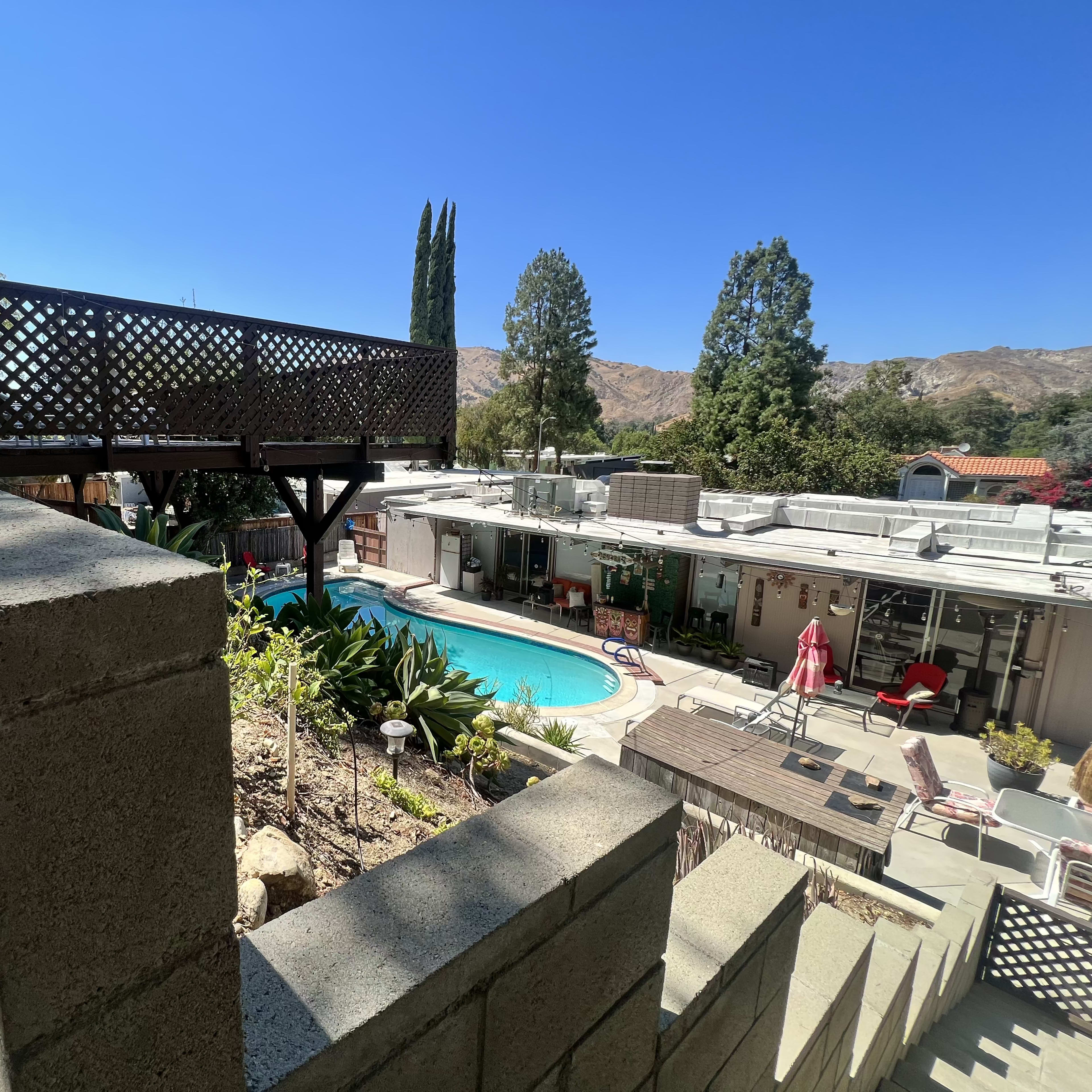 A residential area featuring a pool surrounded by landscaping, with stairs leading up to a deck above.
