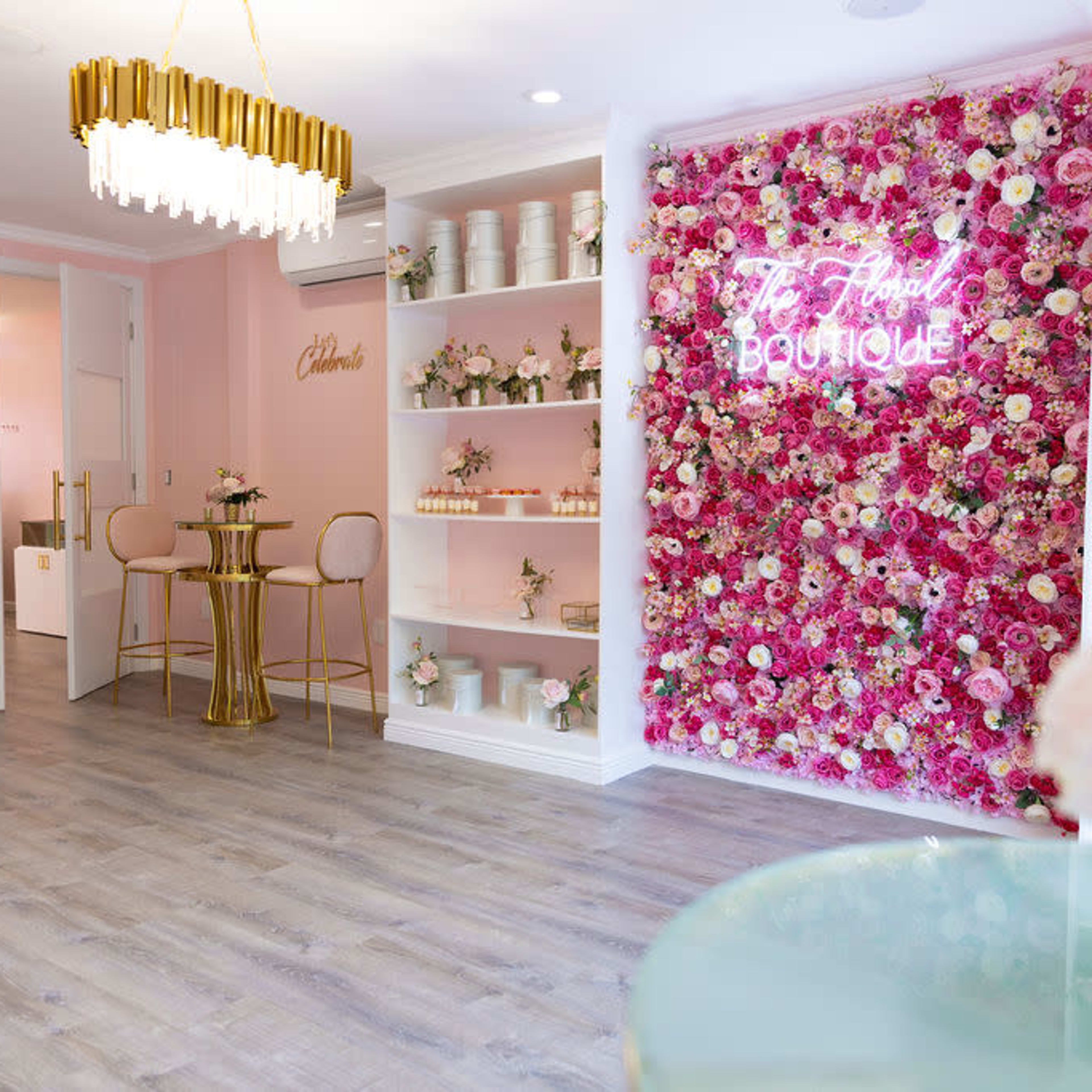 A boutique with pink walls adorned with a floral display, gold furniture, and neatly arranged shelves of products.