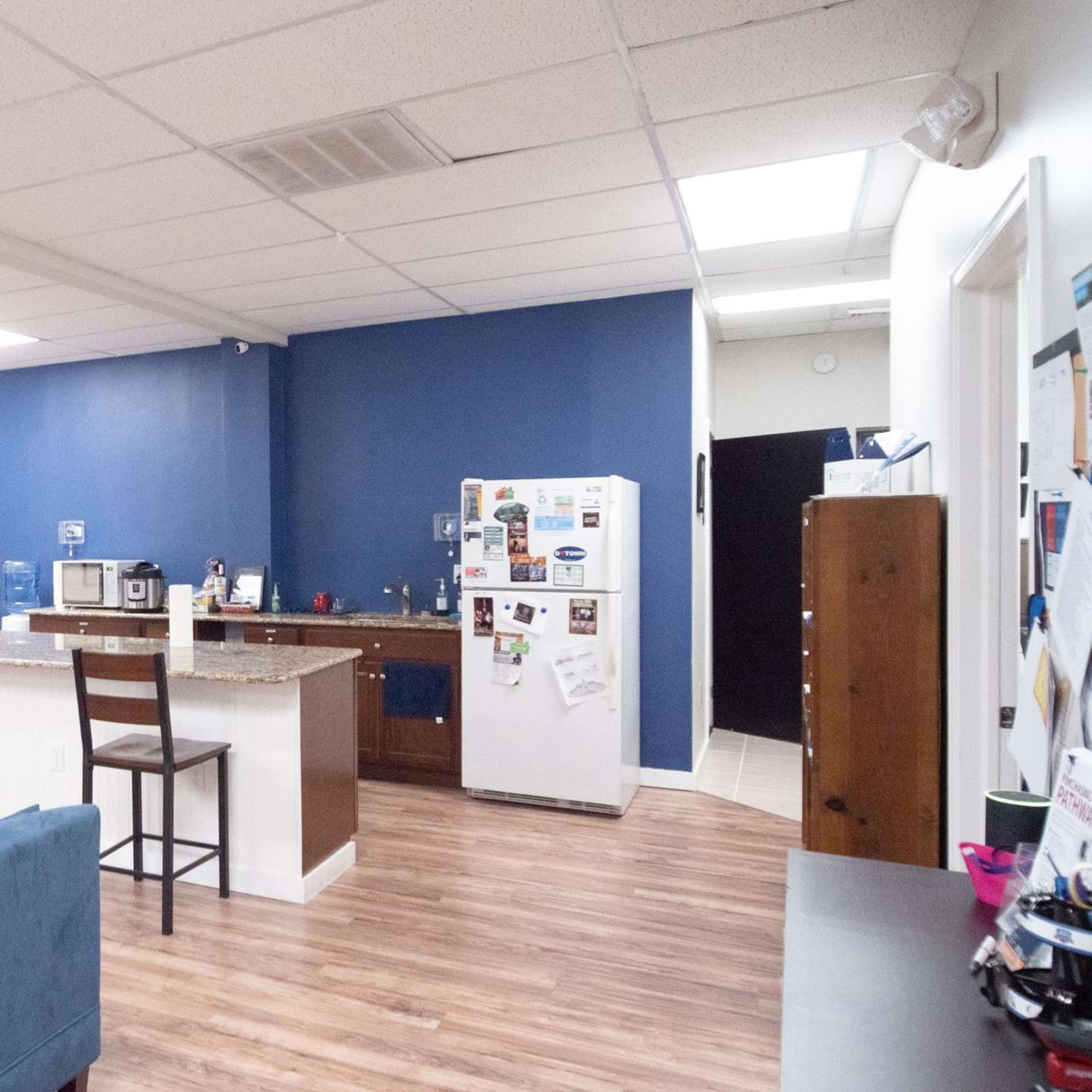 A spacious, modern common area featuring a kitchen with a bar, seating arrangements, and wall decorations.