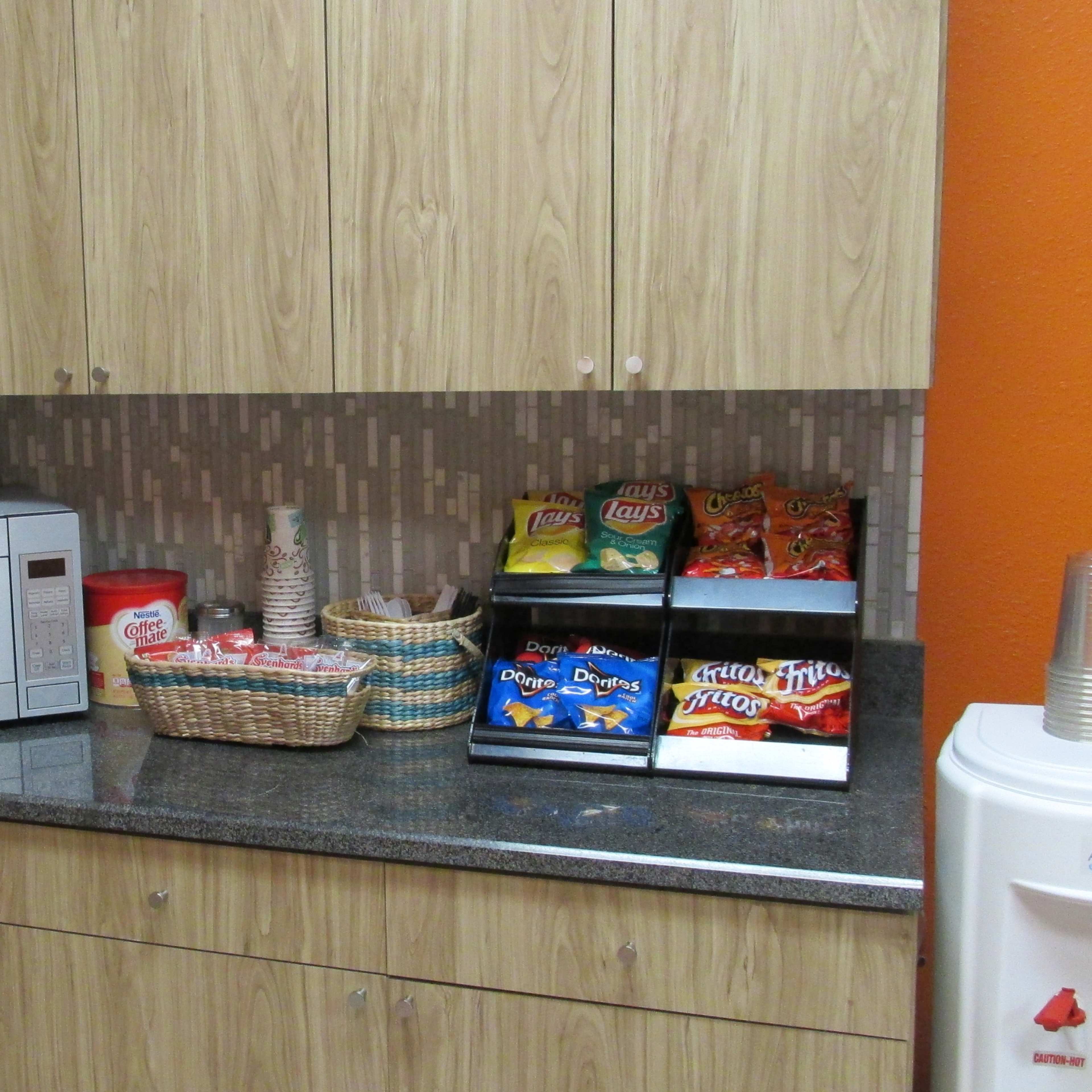 A kitchen countertop features a microwave, coffee maker, and a basket of snacks next to a mini fridge.