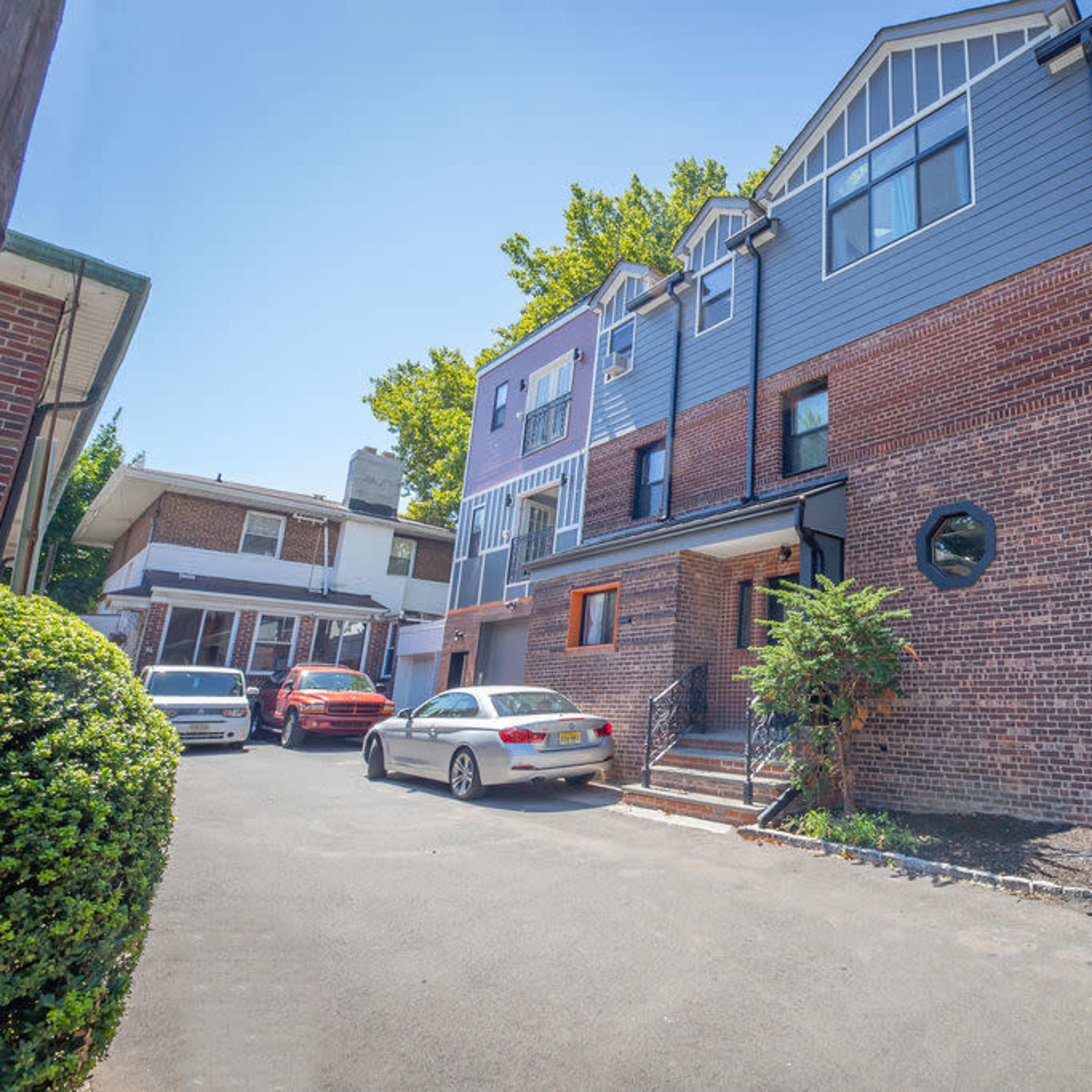 A multi-story brick and gray-clad residential building situated next to a paved driveway with parked cars.