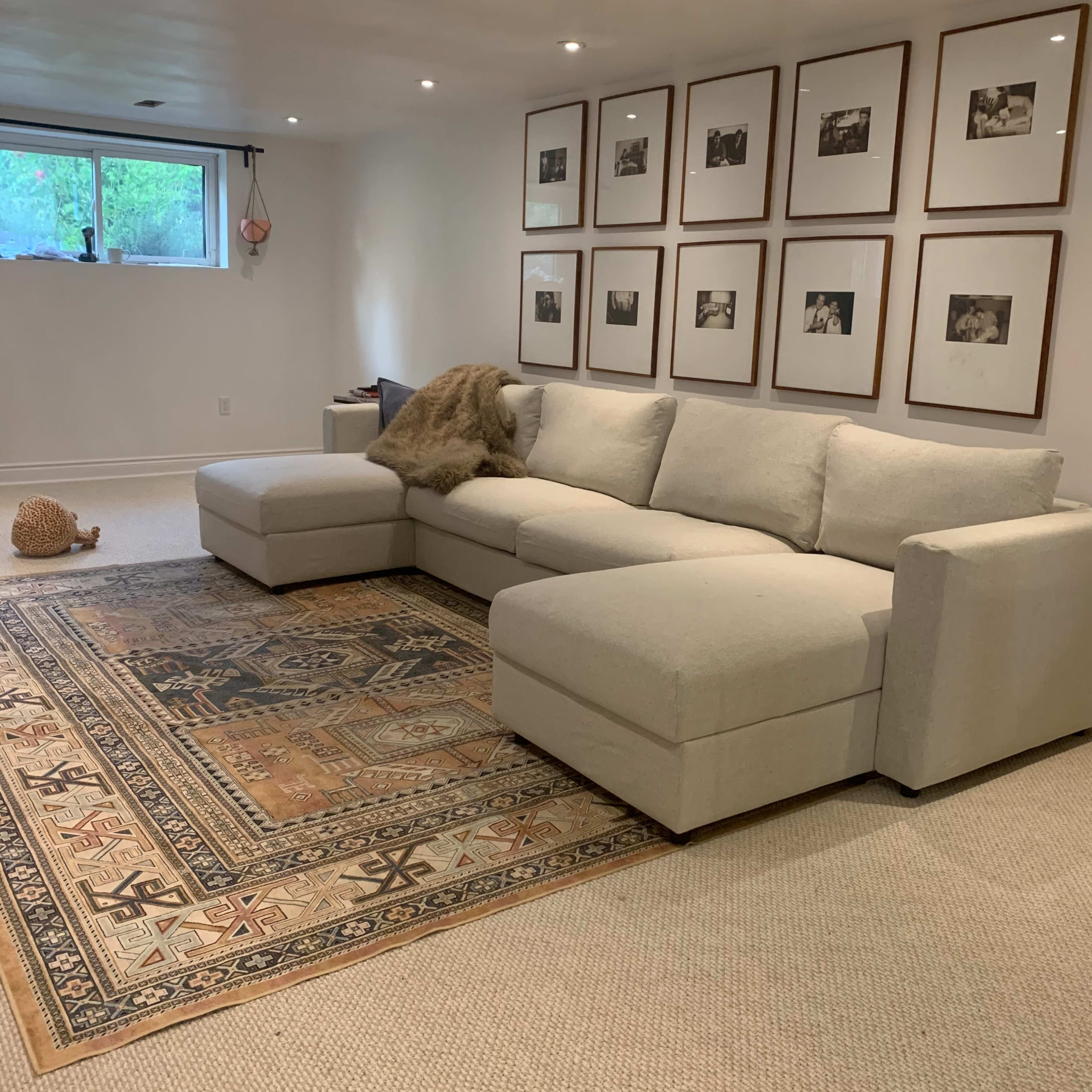 A spacious living area featuring a light-colored sectional sofa, a patterned area rug, and a wall adorned with framed photographs.