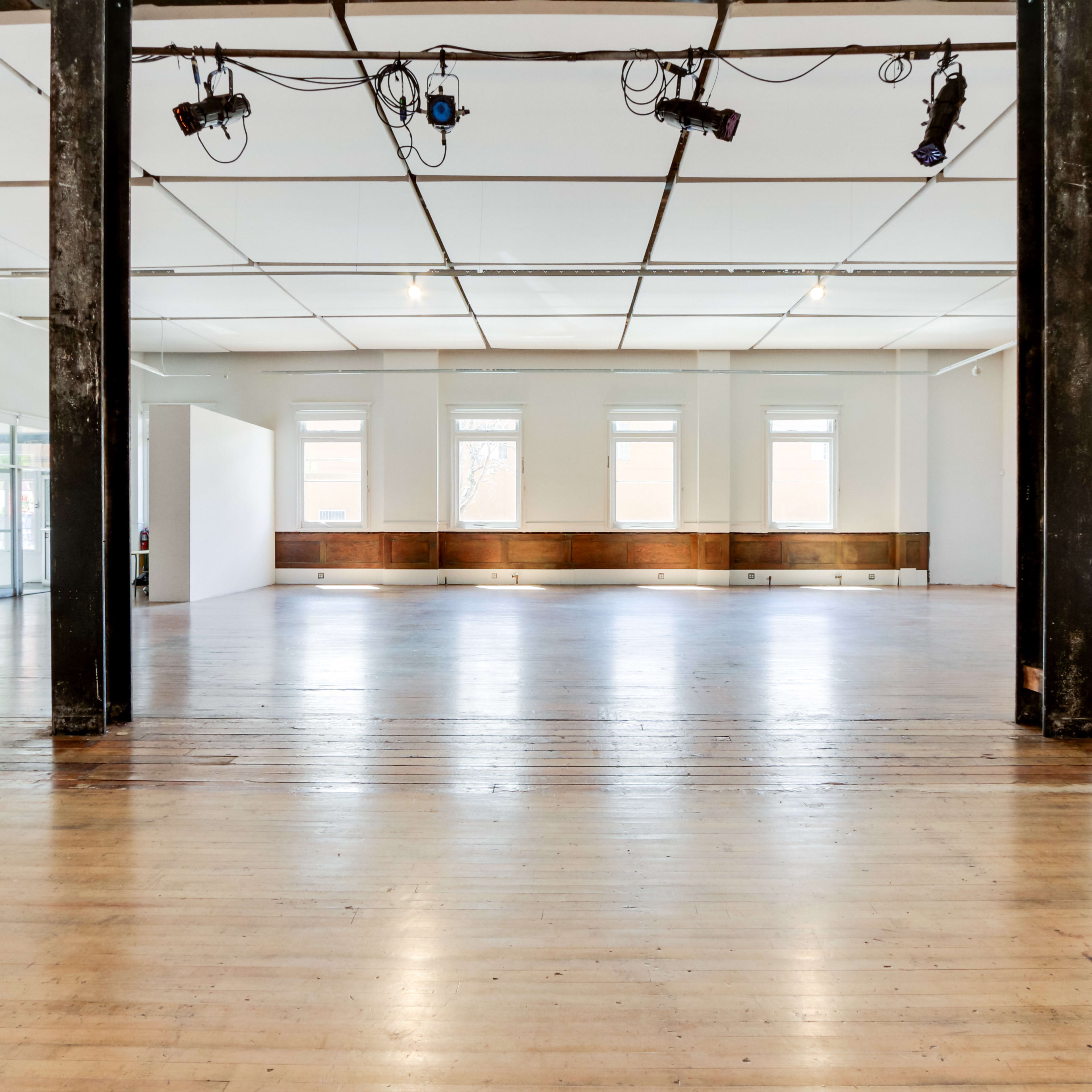 A large, empty room with wooden floors, tall windows, and exposed beams.