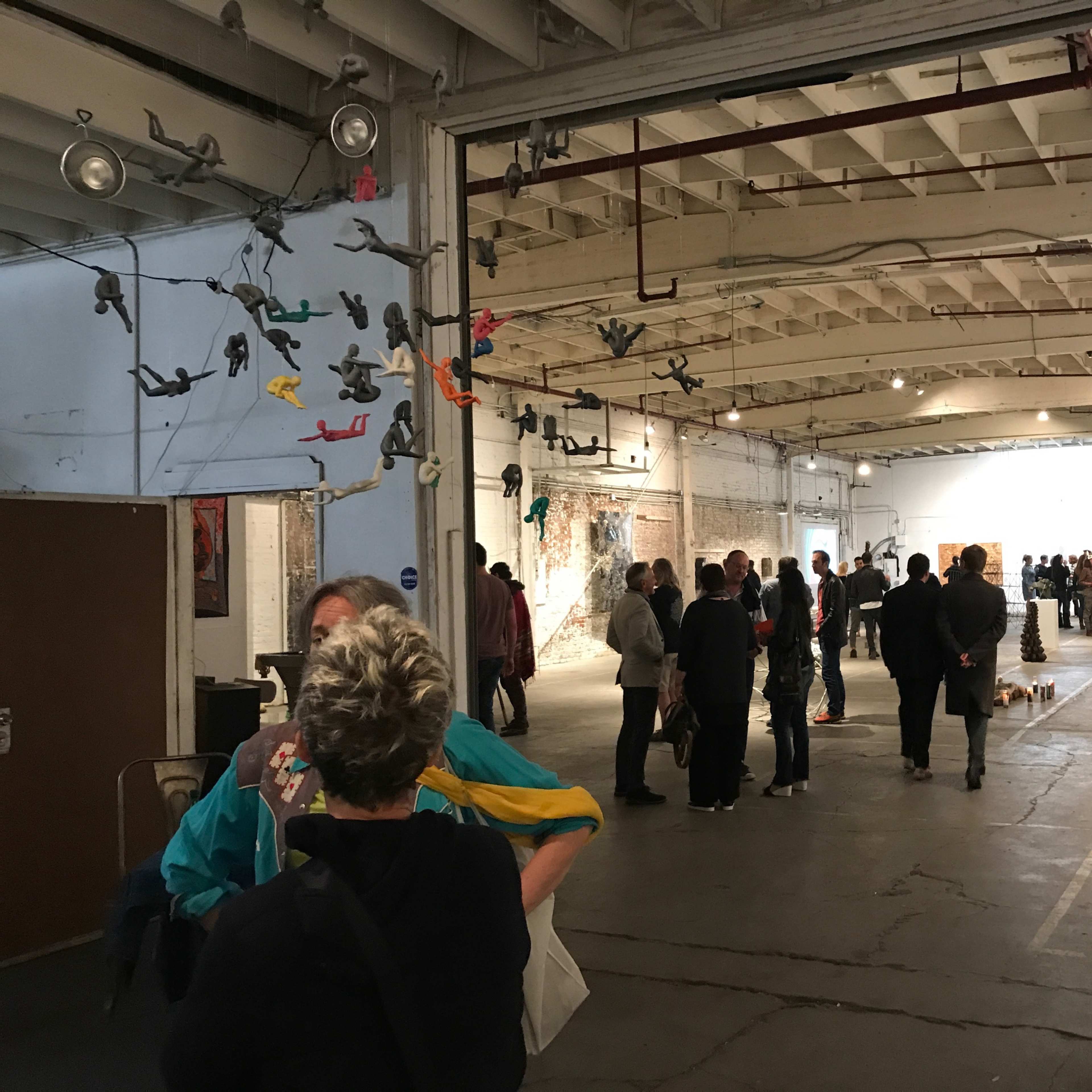 An art gallery event with a crowd of people mingling and viewing artwork in a spacious, well-lit area.
