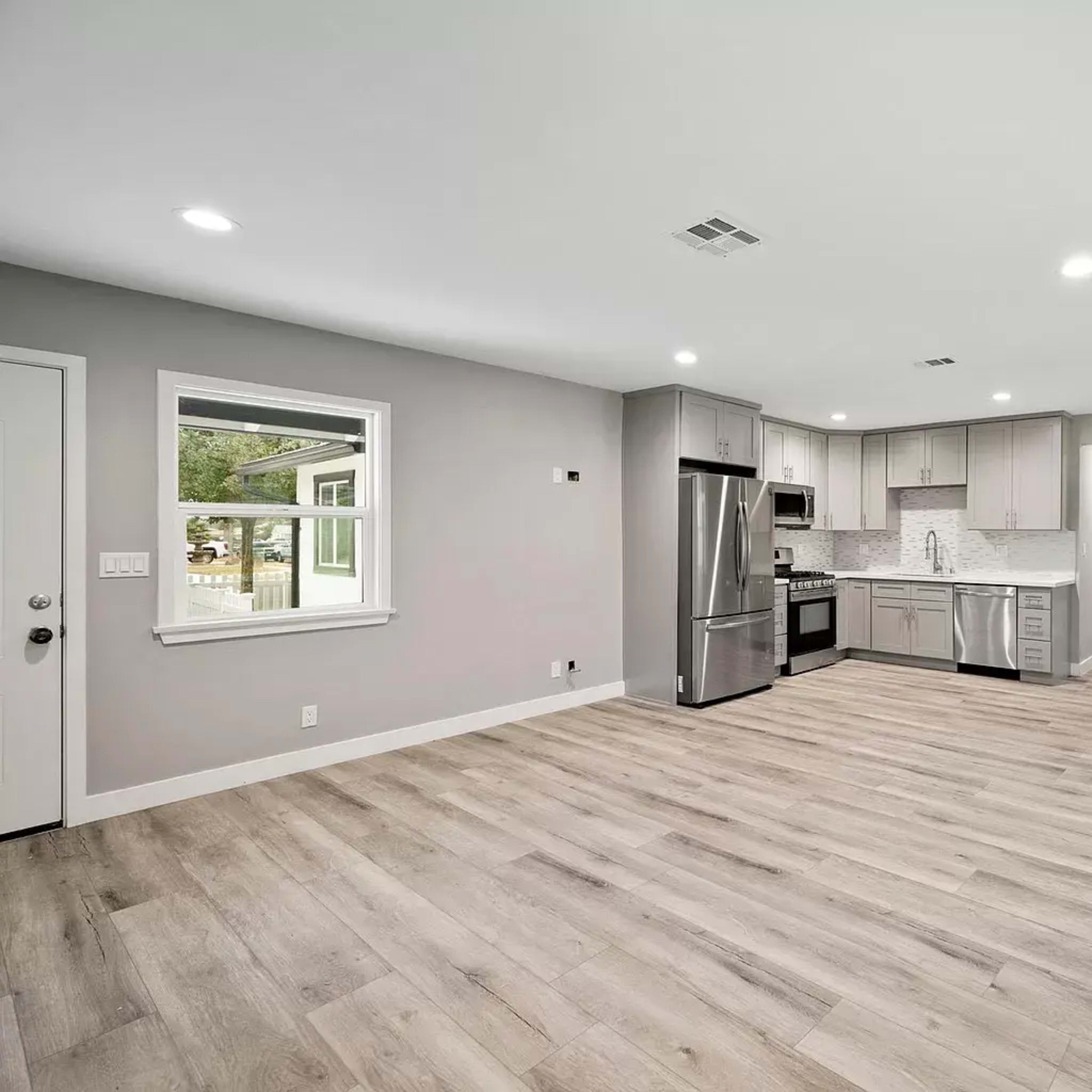 A modern, open-concept kitchen and living area with light wood flooring, gray walls, and stainless steel appliances.