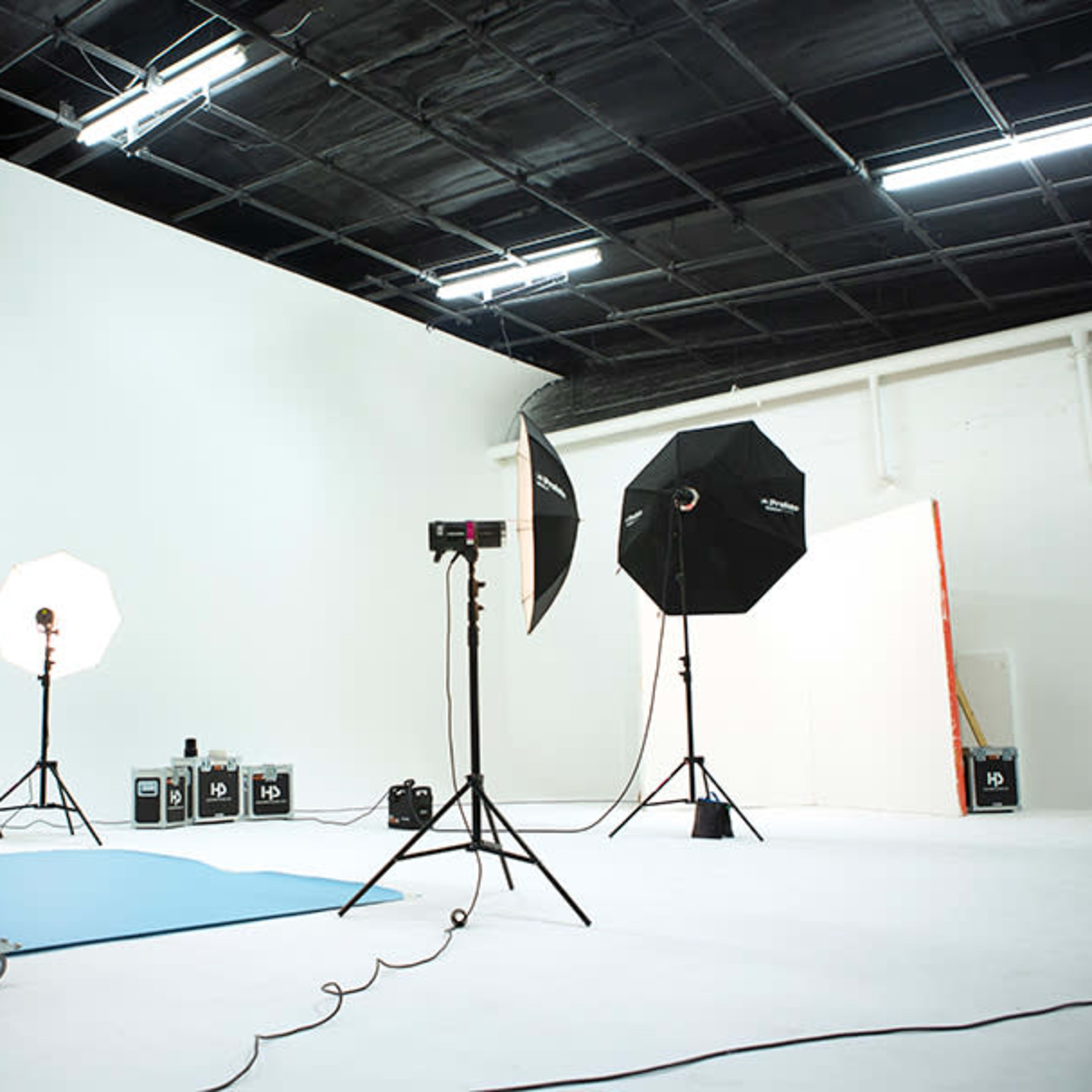 A photography studio with a white backdrop, lighting equipment, and a blue fabric on the floor.
