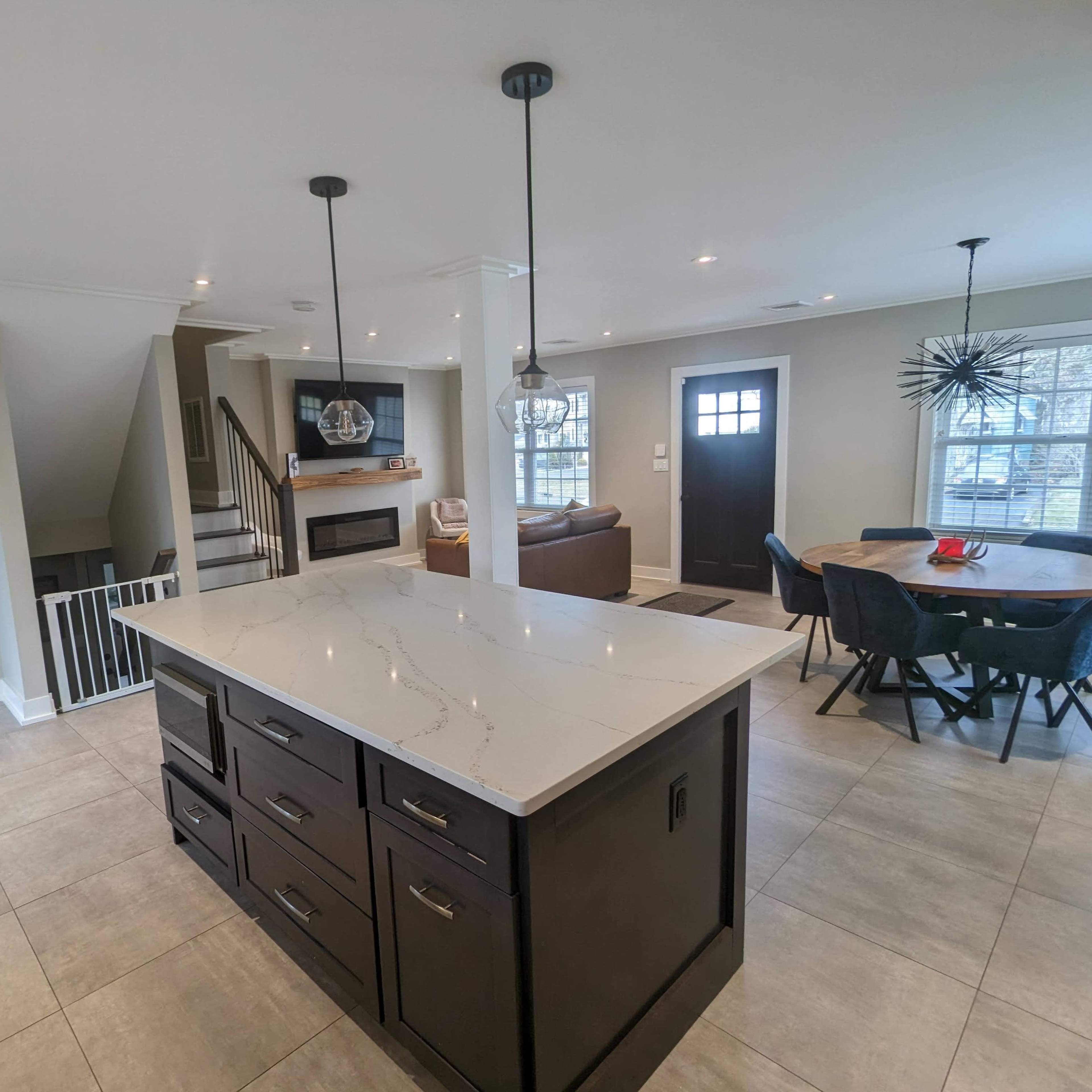 A modern kitchen features a central island, a dining area with a round table, and a staircase leading to a living space.