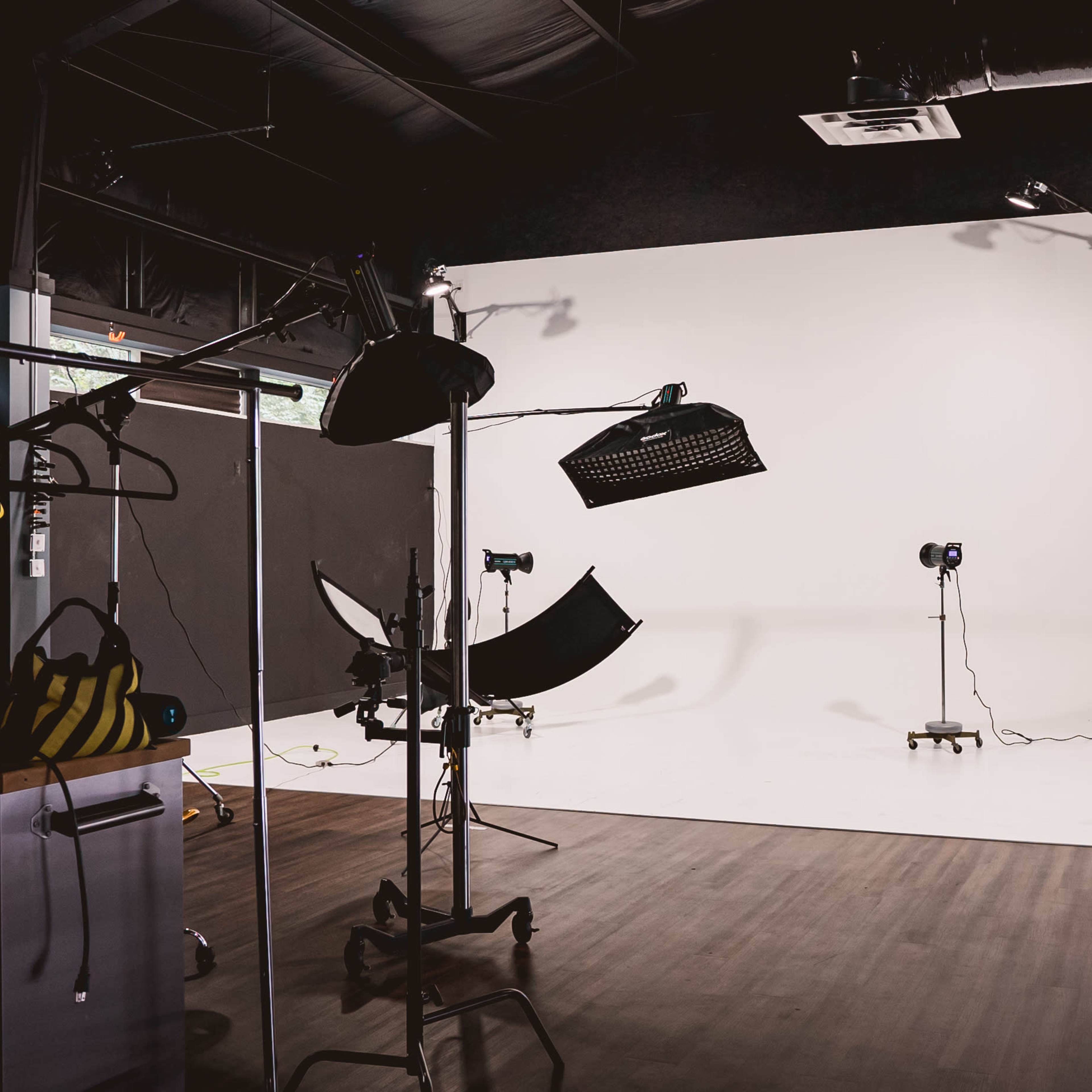 A photography studio features a backdrop setup with lighting equipment and a large white wall.