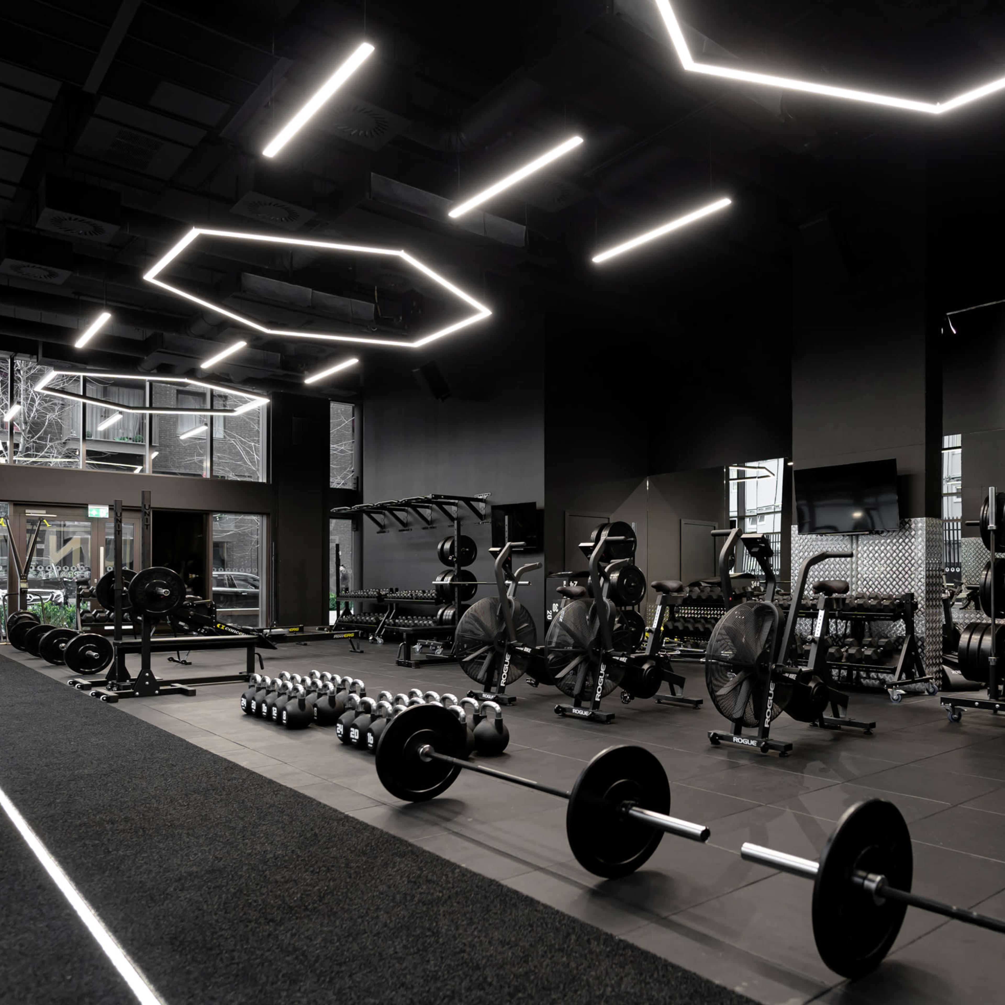 The gym features black walls, large mirrors, and various weightlifting equipment arranged neatly along the space.