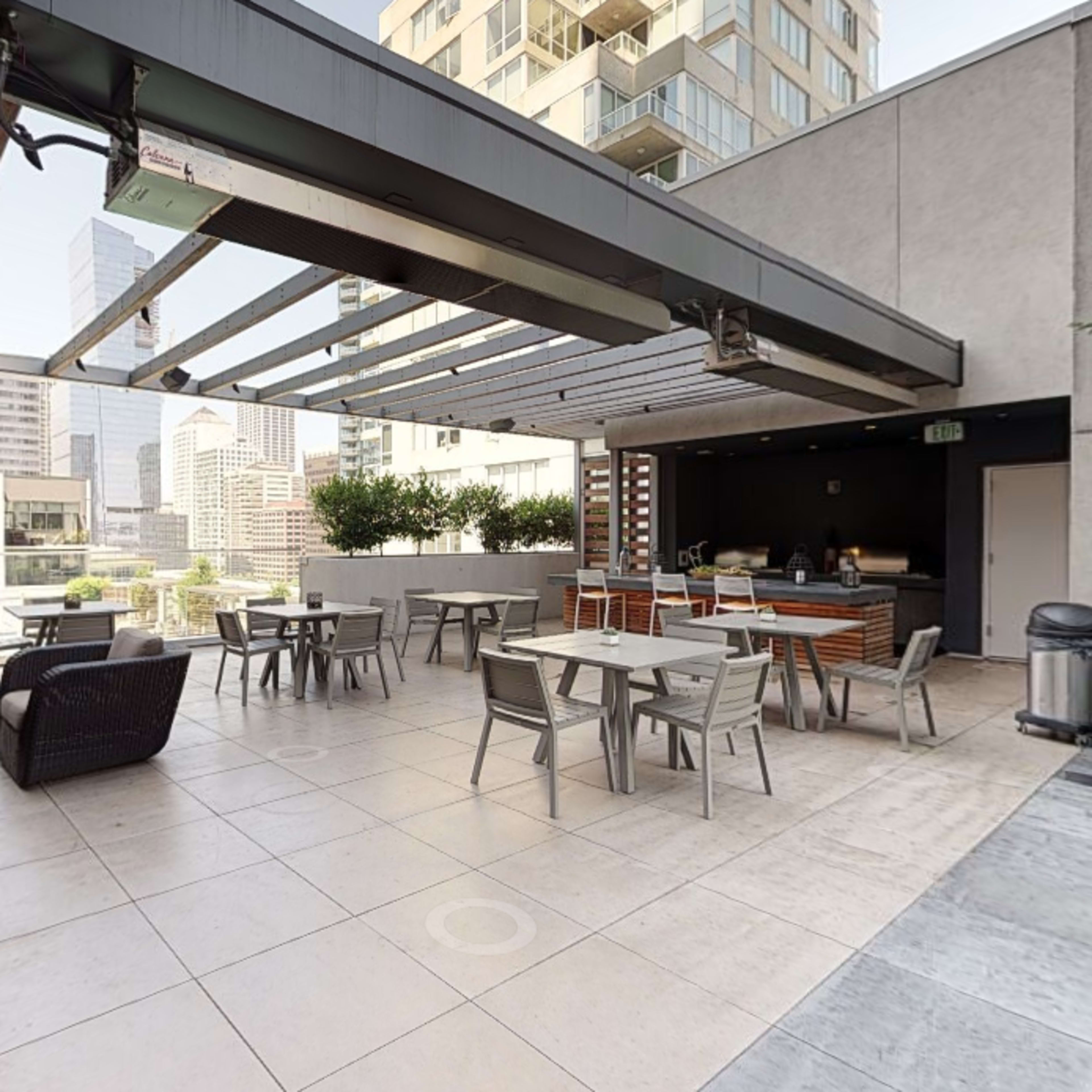 A rooftop terrace with outdoor seating, tables, and a view of surrounding buildings.