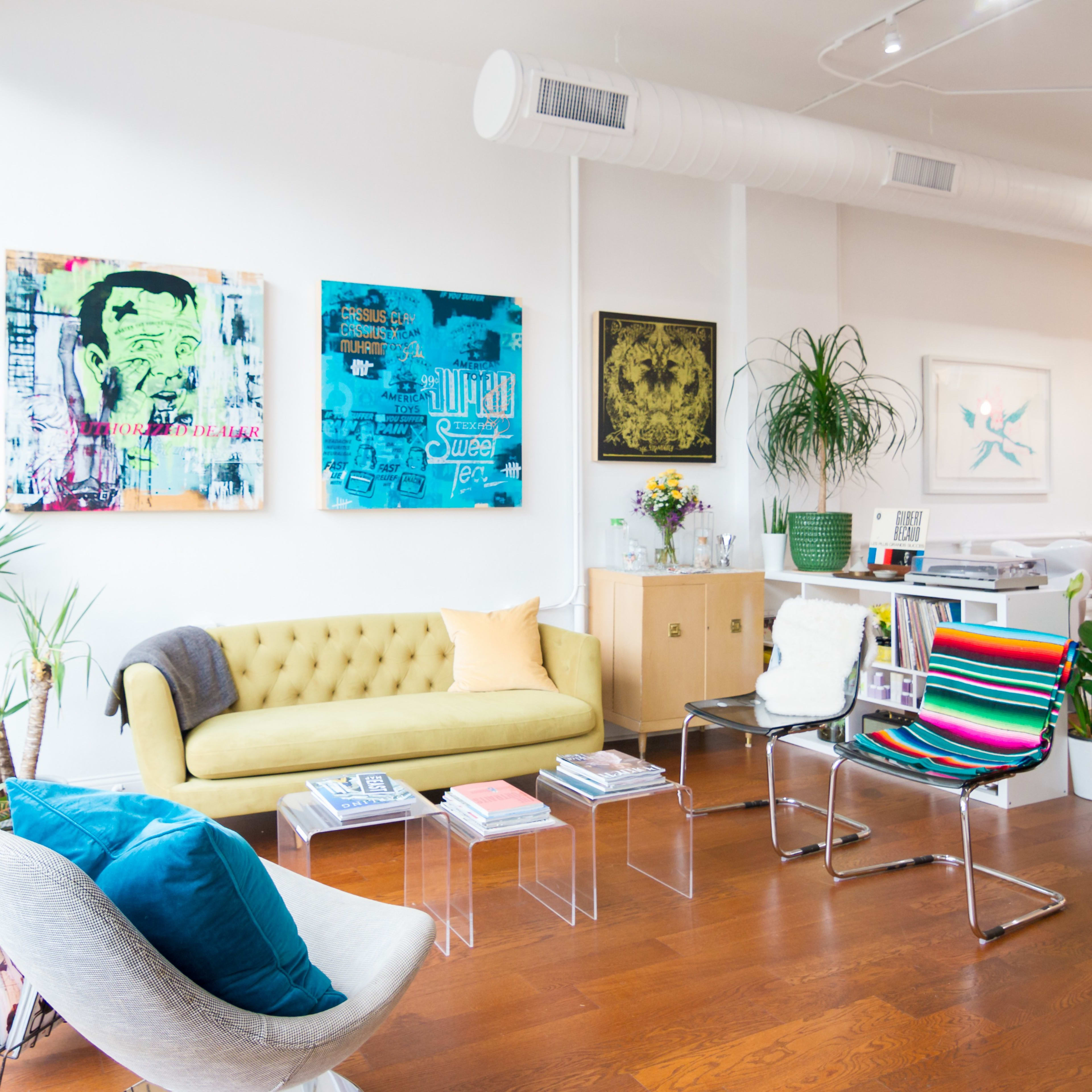 A bright, modern living space featuring a yellow sofa, colorful wall art, a glass table, and various plants.