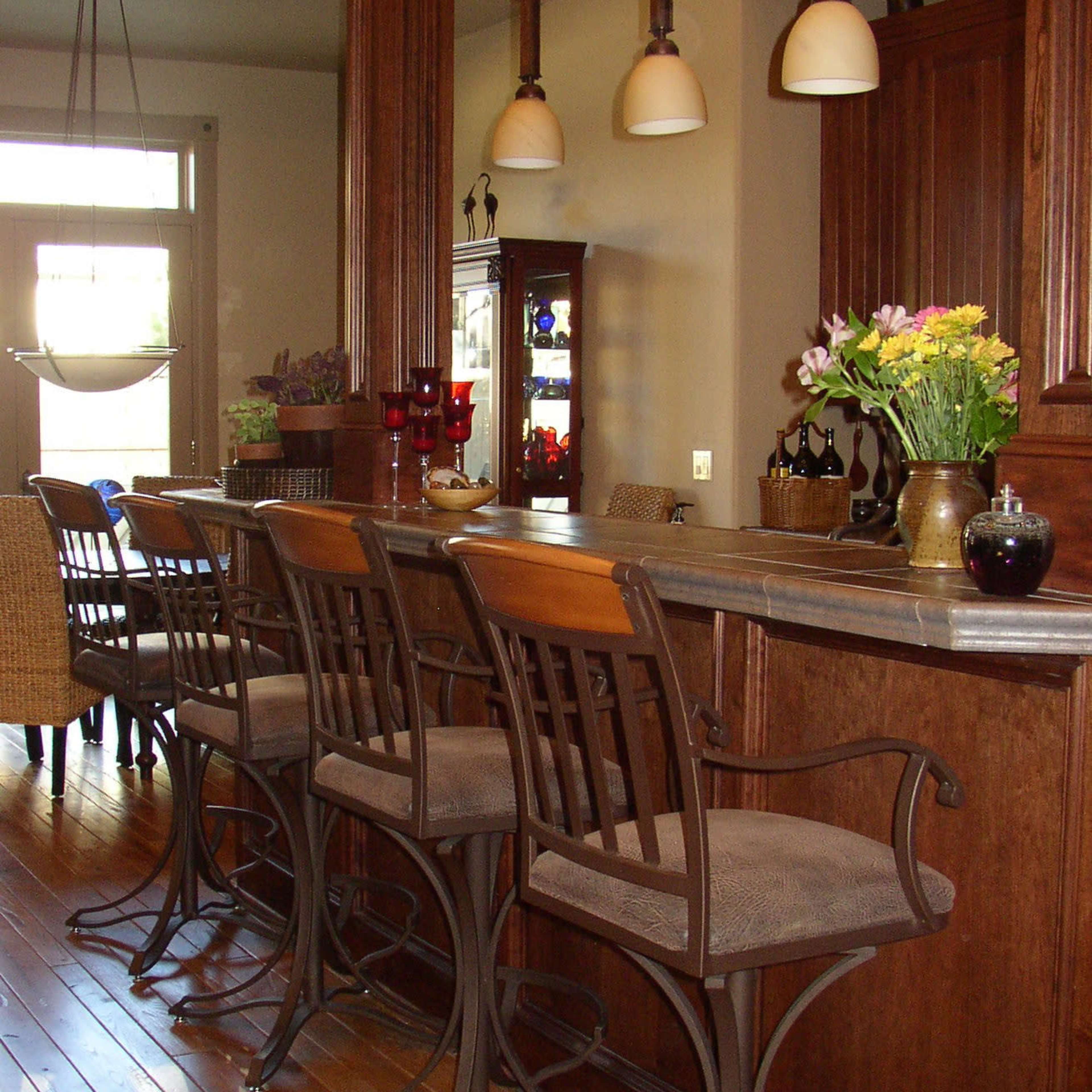 A kitchen bar area with several high-backed stools arranged in front of a counter, illuminated by hanging pendant lights.
