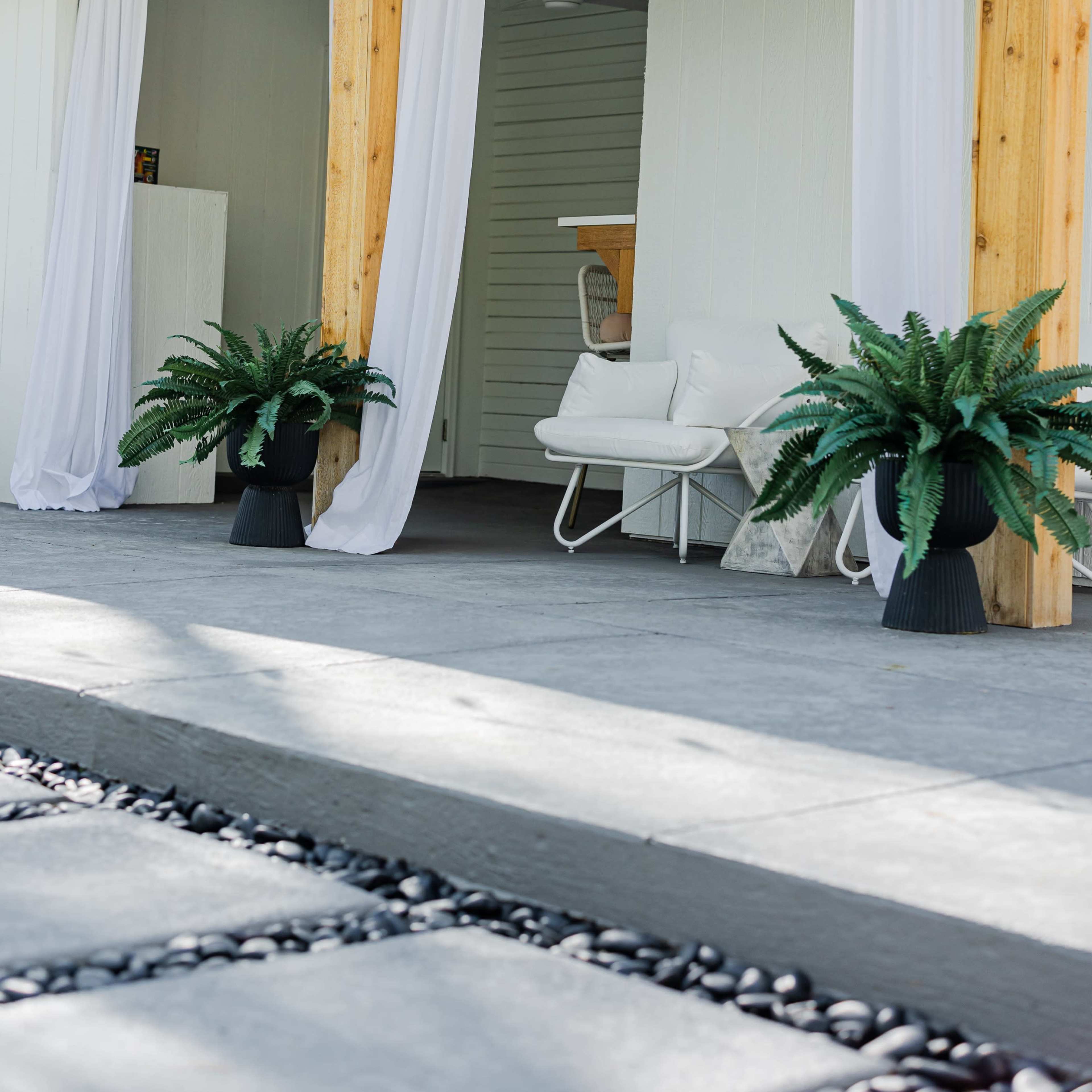 A modern entrance area of a house with white curtains, wooden pillars, and potted ferns on either side.