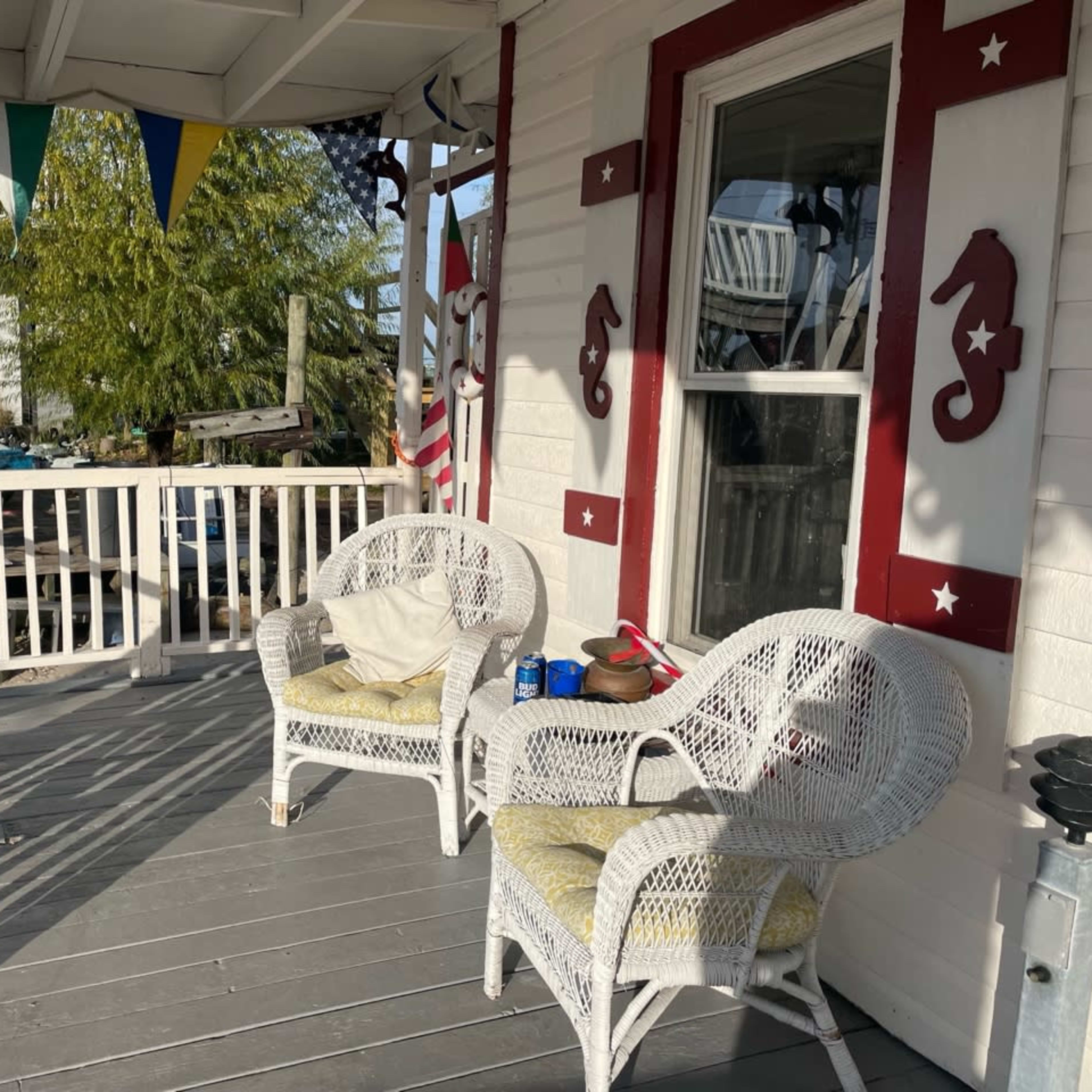 A covered porch with two wicker chairs and a small table, adorned with decorative seahorse designs and colorful bunting overhead.