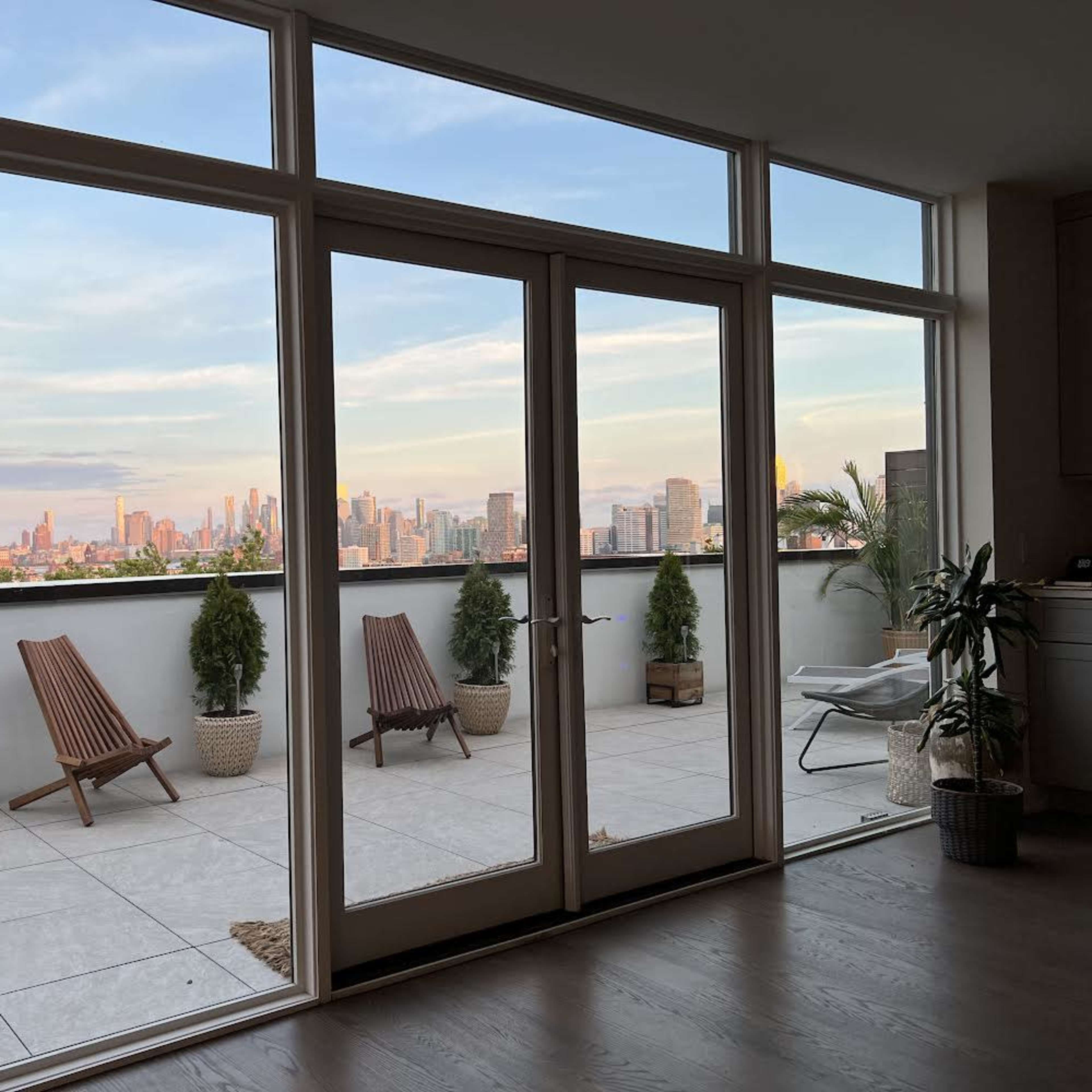 A modern indoor space with large glass doors leading to a terrace that overlooks a city skyline.