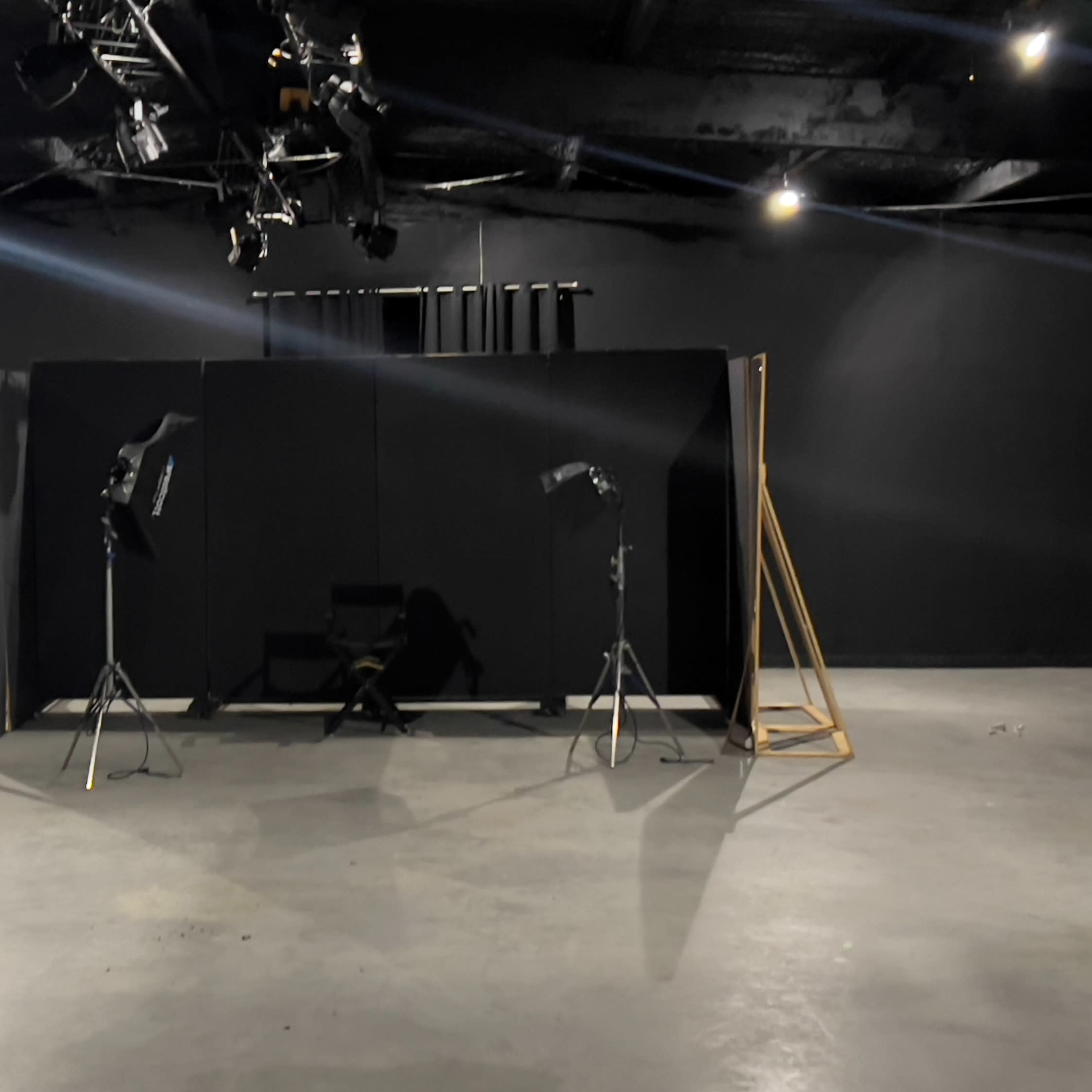 An empty studio space with a black backdrop, two lighting stands, and a chair positioned in front of the backdrop.