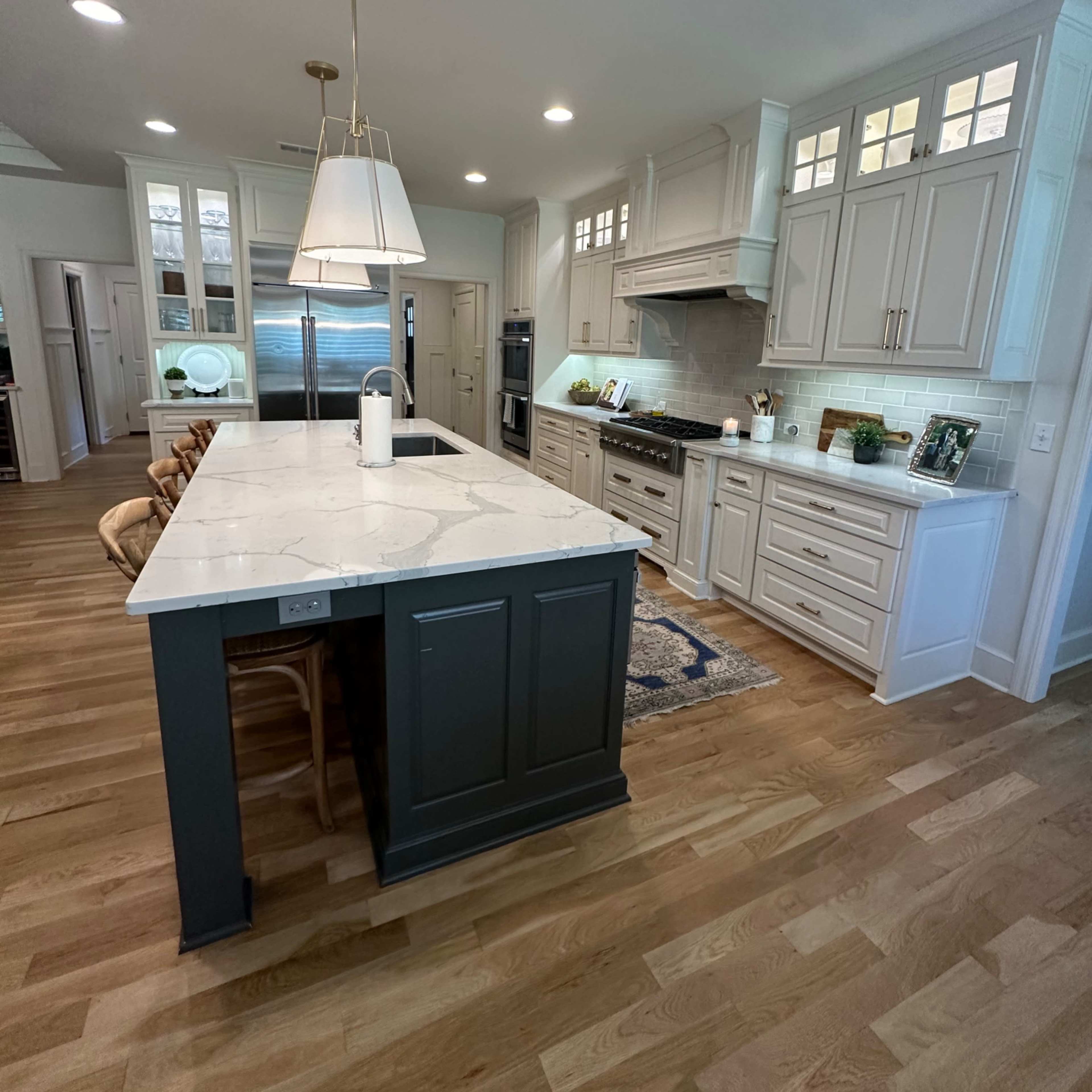 A modern kitchen featuring a large island with a white countertop, light cabinetry, and wooden flooring.