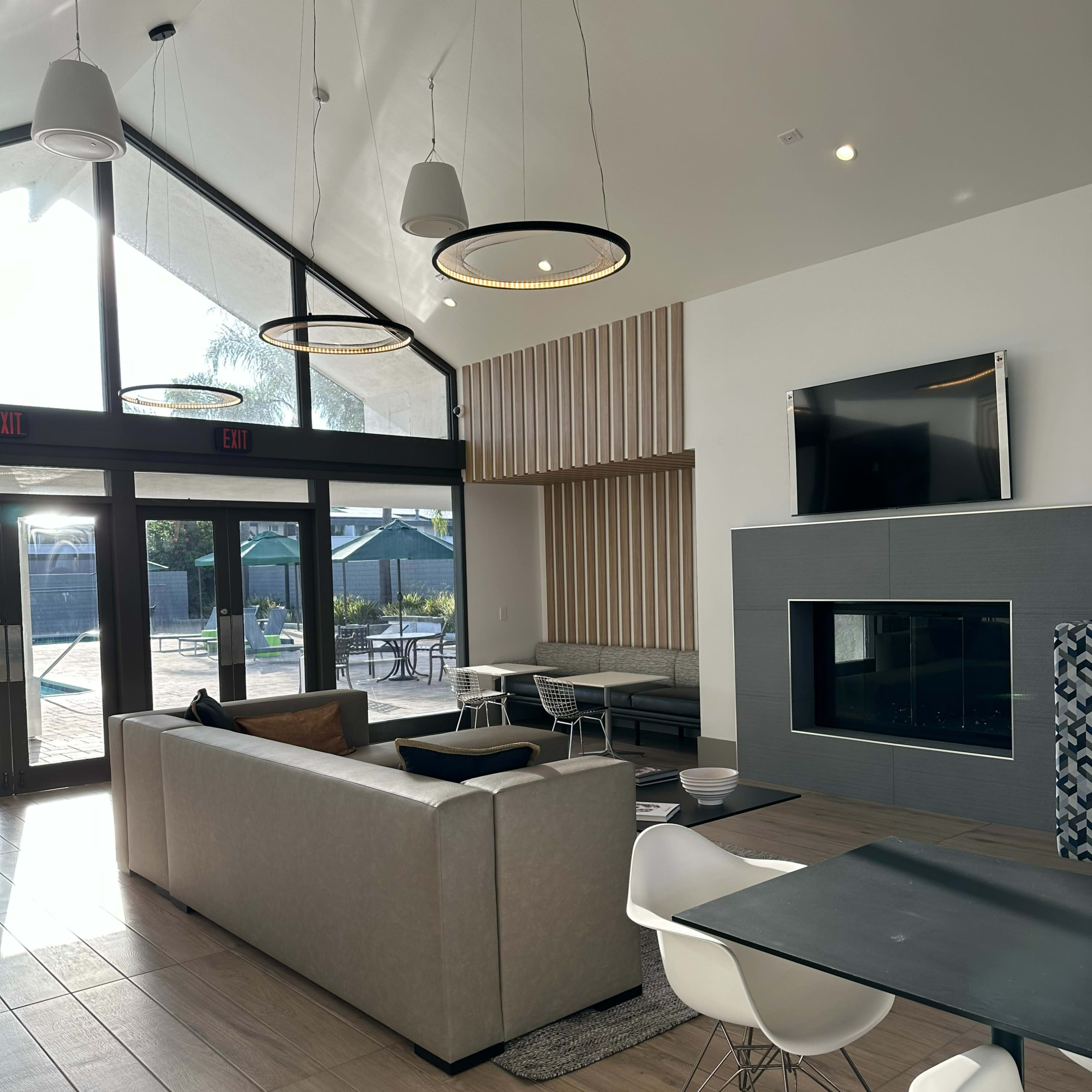 A modern lounge area with a tall ceiling, a sofa, a dining table, and a large window overlooking an outdoor space.