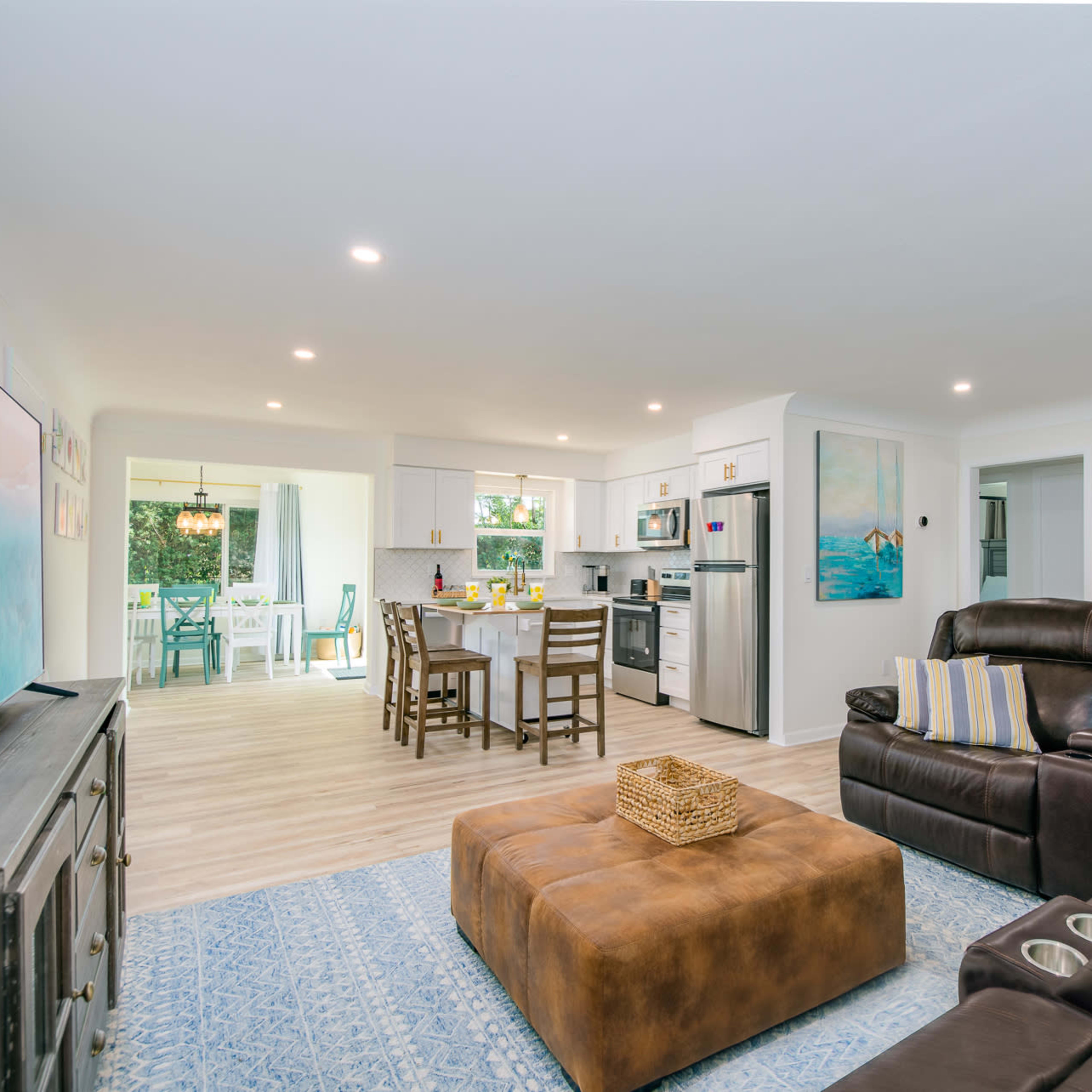 A modern living room features a sectional couch, a coffee table, and an open kitchen area with dining space and access to an outdoor patio.